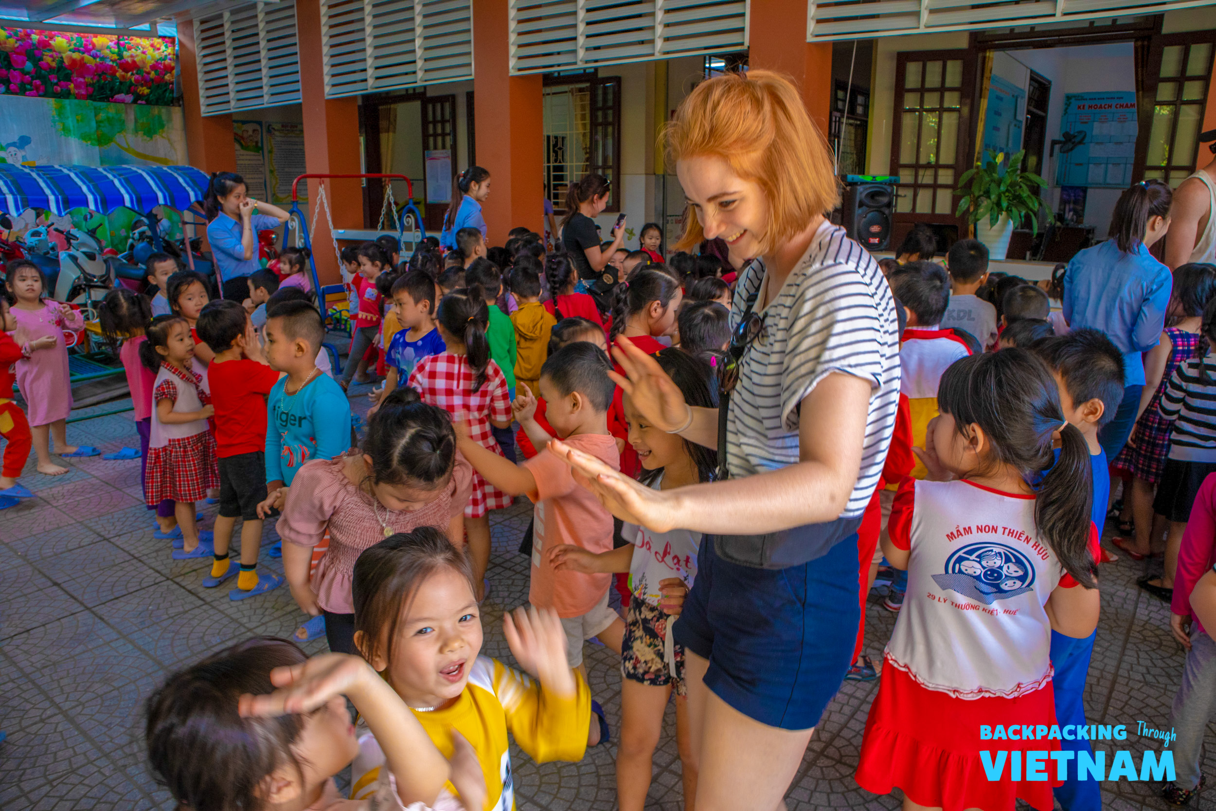 A smiling backpacker plays a game with many happy children at a school in Hue, Vietnam.