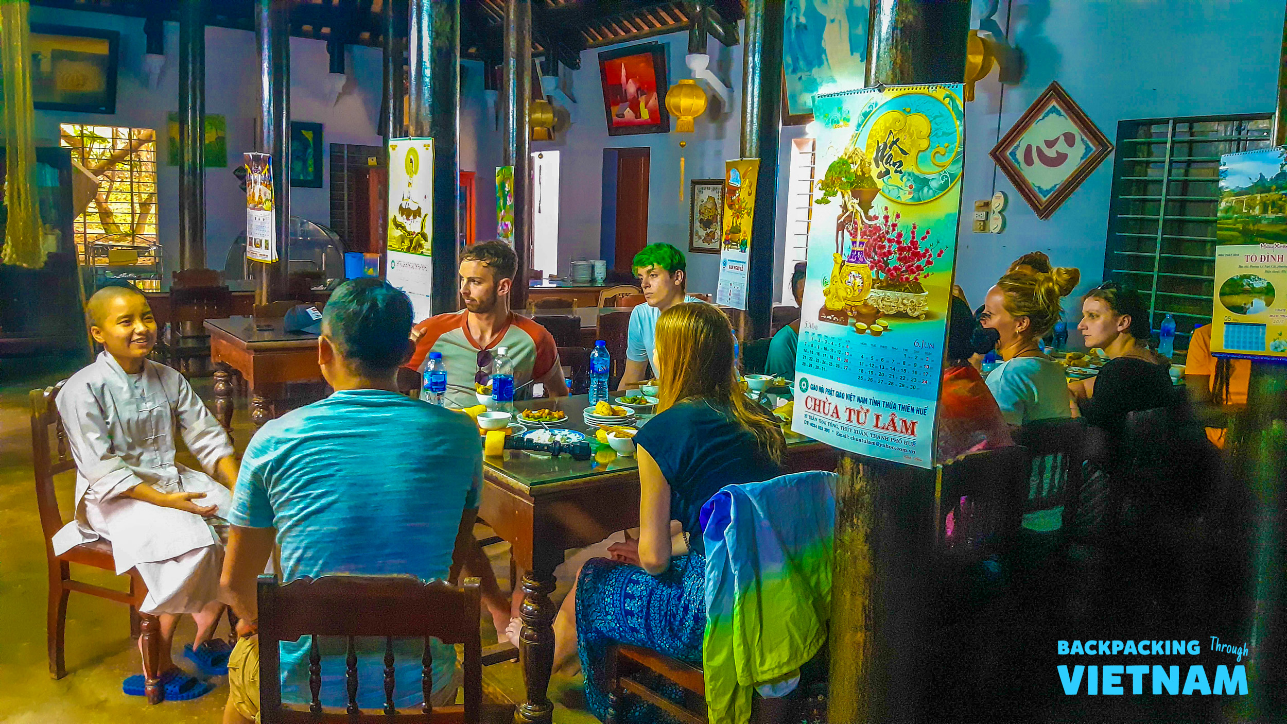 Backpackers share a meal and conversation with a local in a traditional dining room in Hue.
