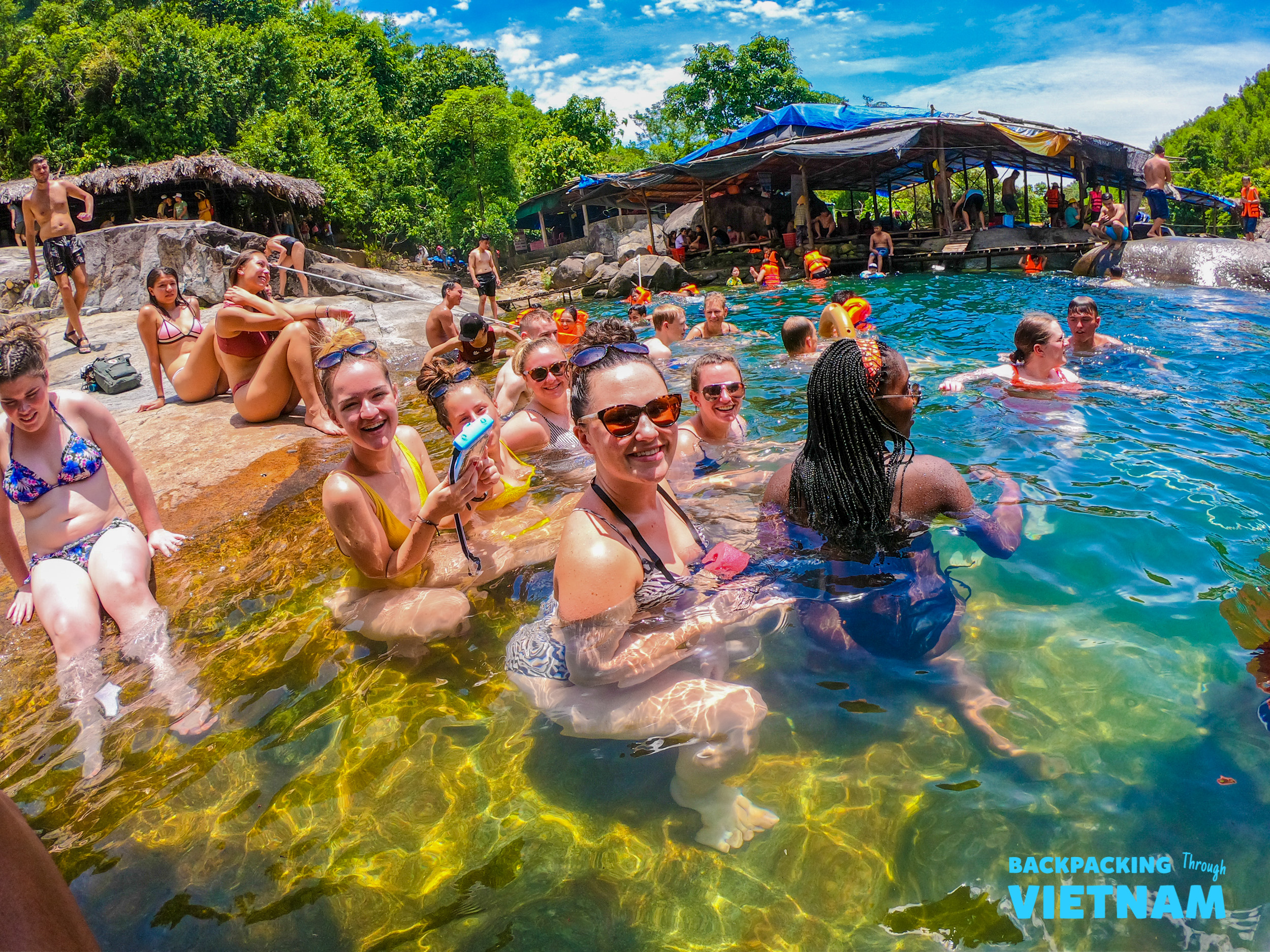 Happy backpackers swim and relax in a clear natural spring on a sunny day in Hoi An.