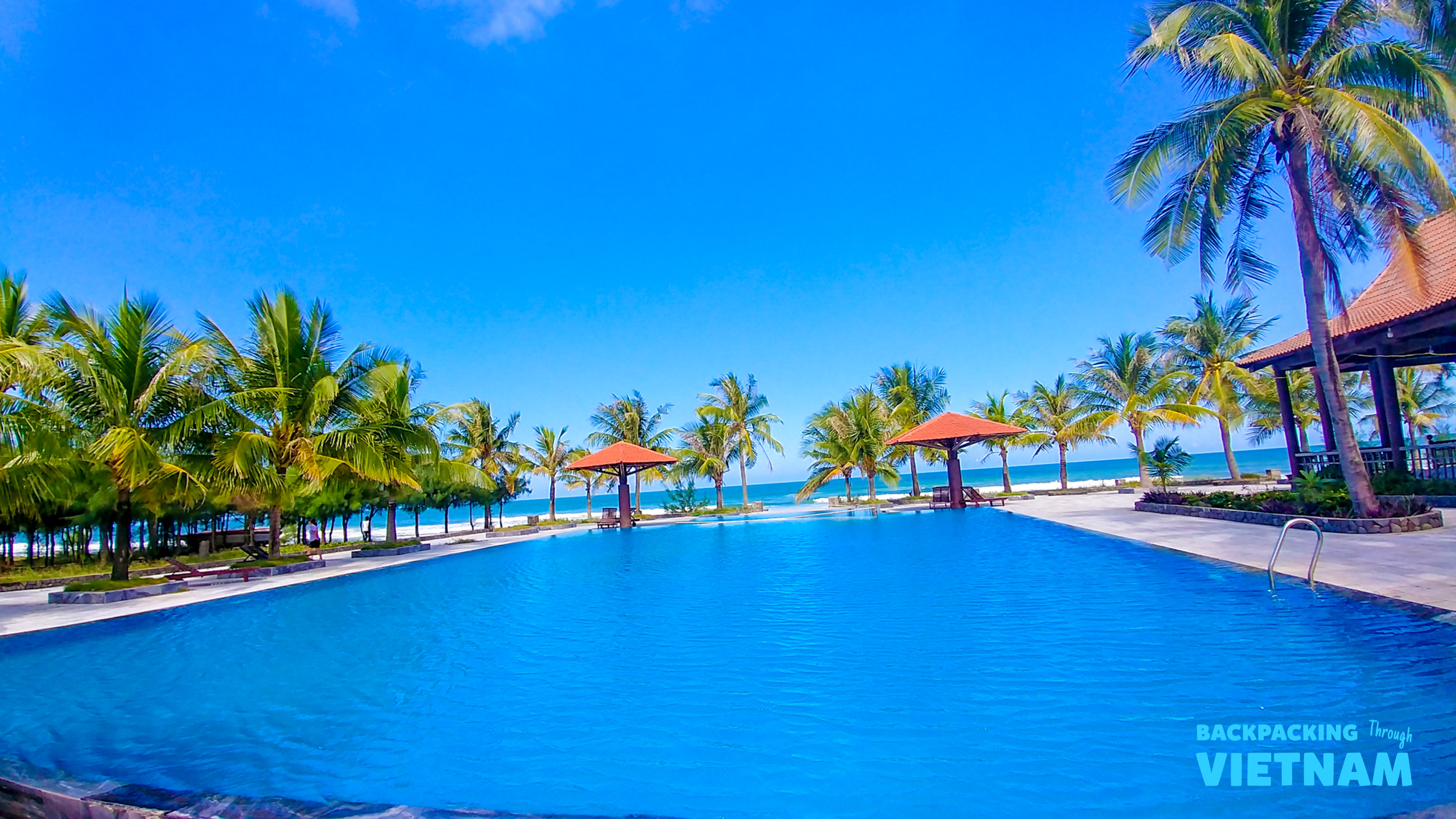 A large, inviting swimming pool with palm trees and ocean views in sunny Hoi An, Vietnam.