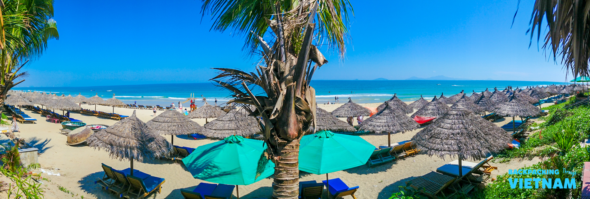 Sunny day with white sands, straw umbrellas, and blue ocean at An Bang Beach, Hoi An.