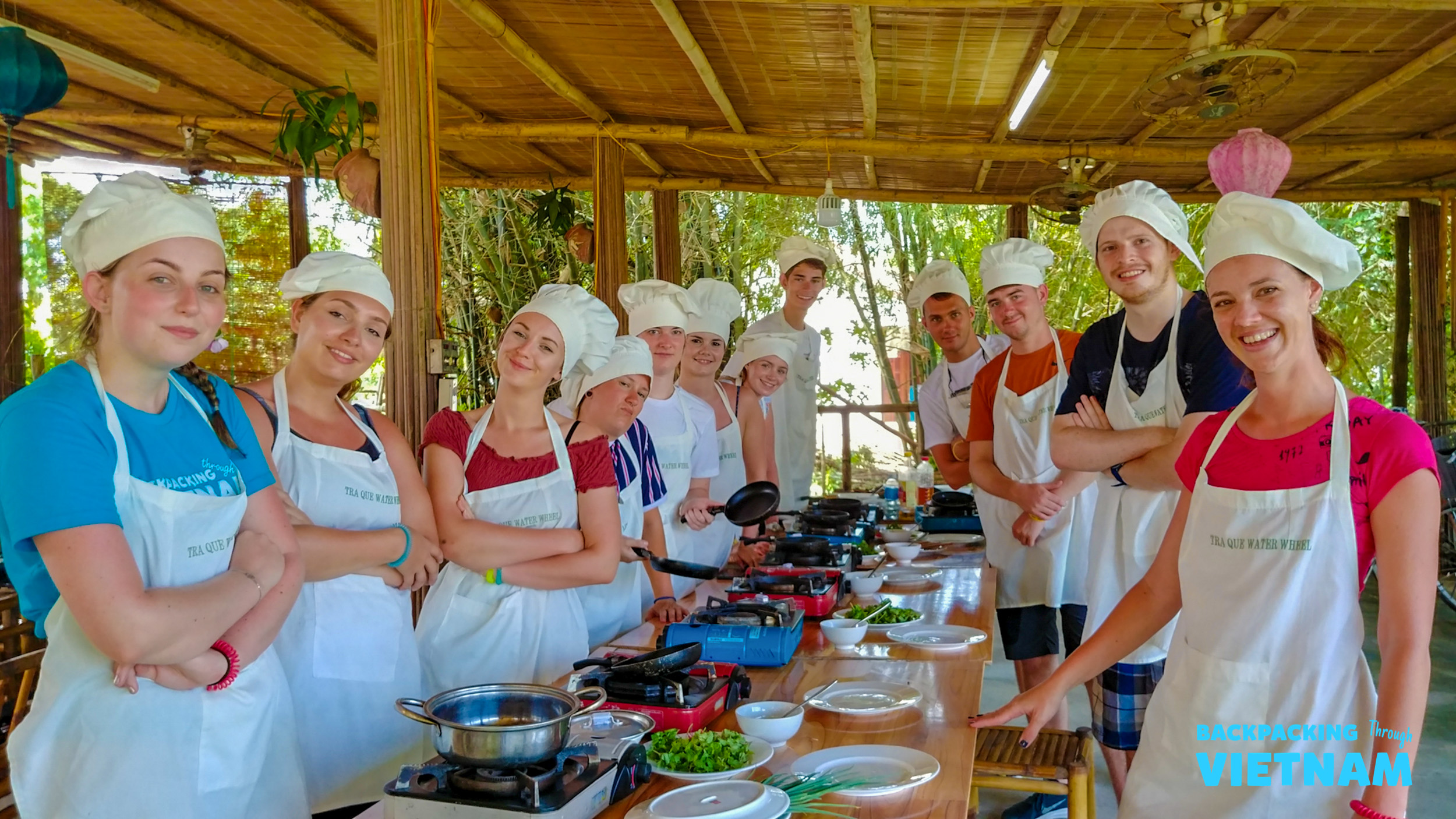Happy backpackers in chef hats and aprons learning to cook local dishes in Hoi An.