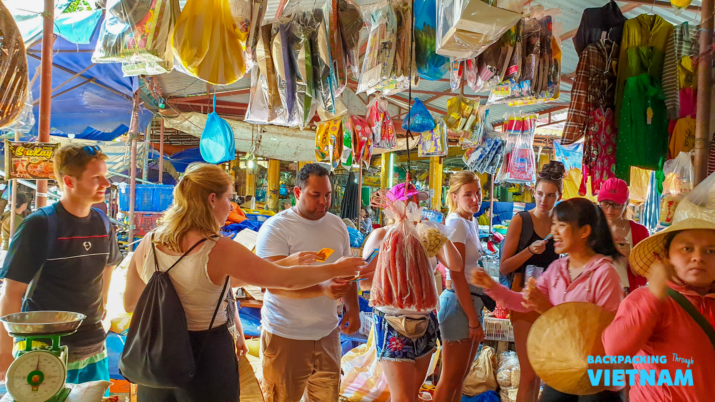 Travelers engage with local vendors at a bustling, colorful market in Hoi An, Vietnam.