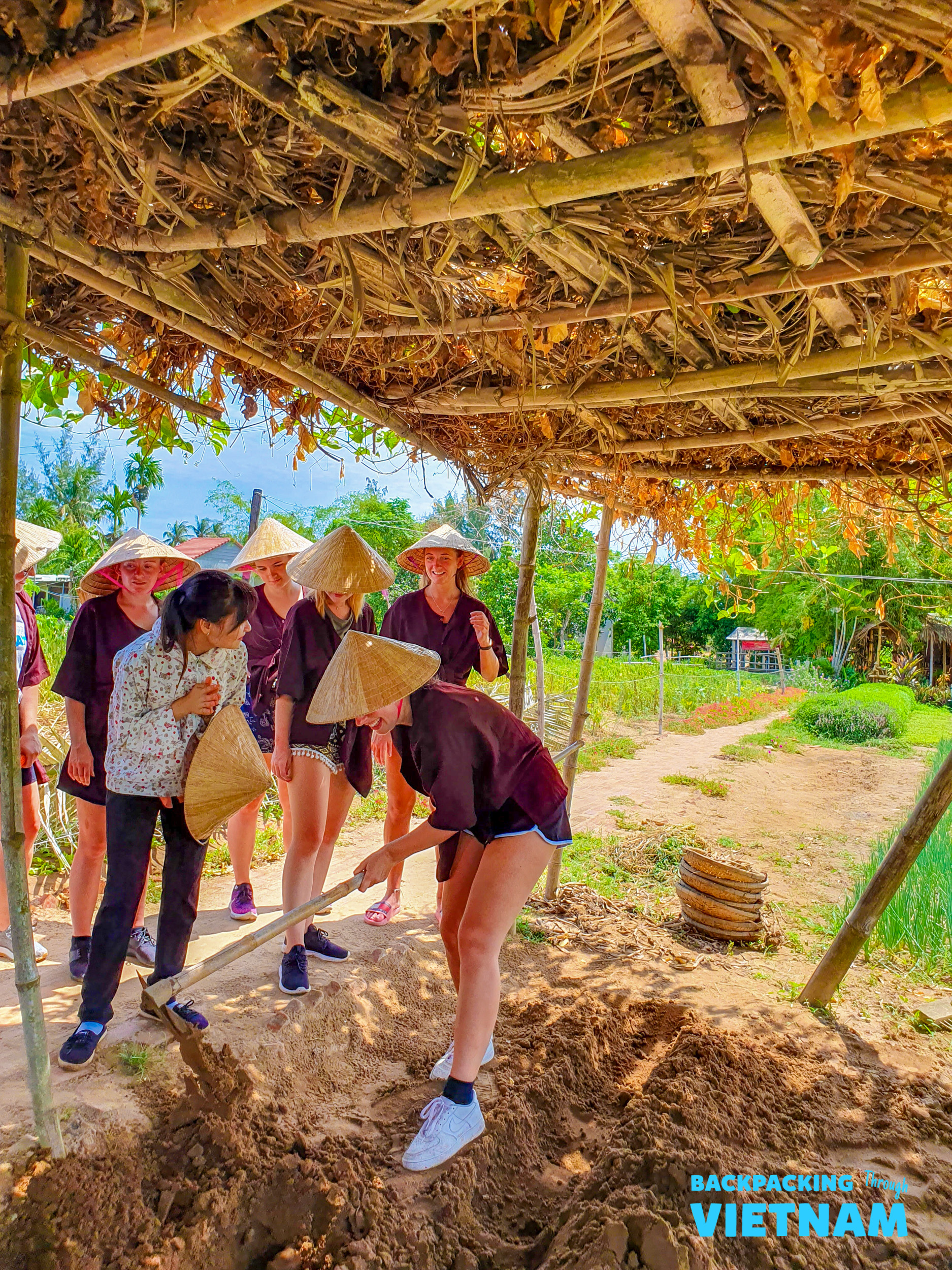 Travelers in conical hats learn to dig at an organic farm in Hoi An, Vietnam.