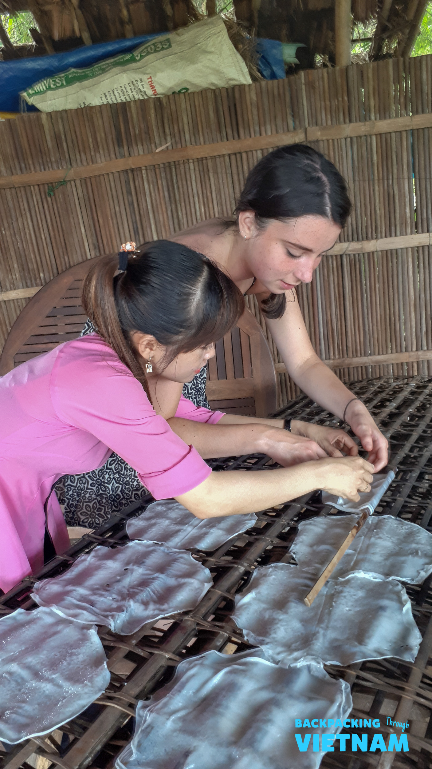 A local woman teaches a tourist to make fresh Vietnamese rice paper in Hoi An.
