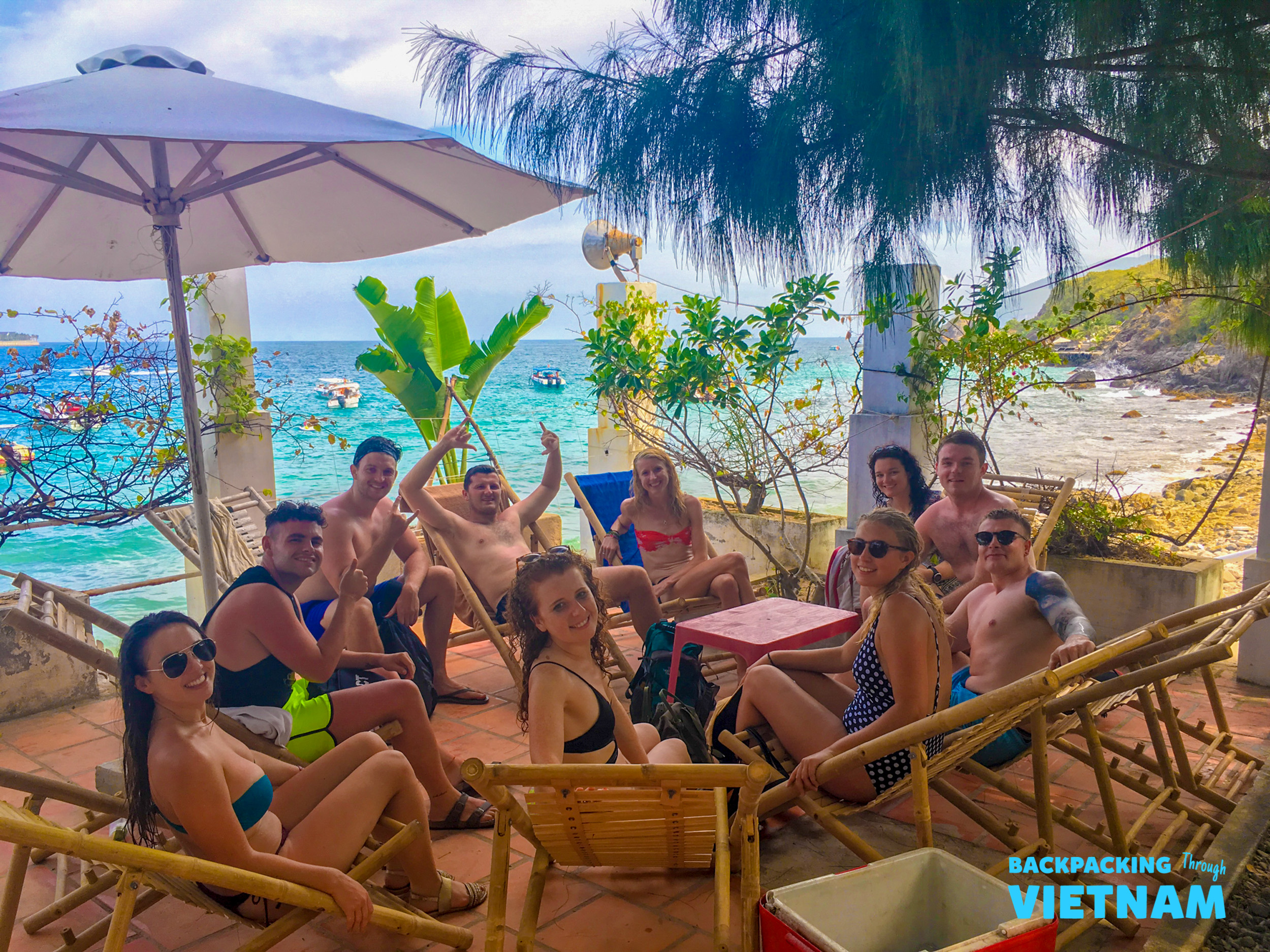 Smiling backpackers relax on a sunny patio overlooking the beautiful blue ocean in Nha Trang.