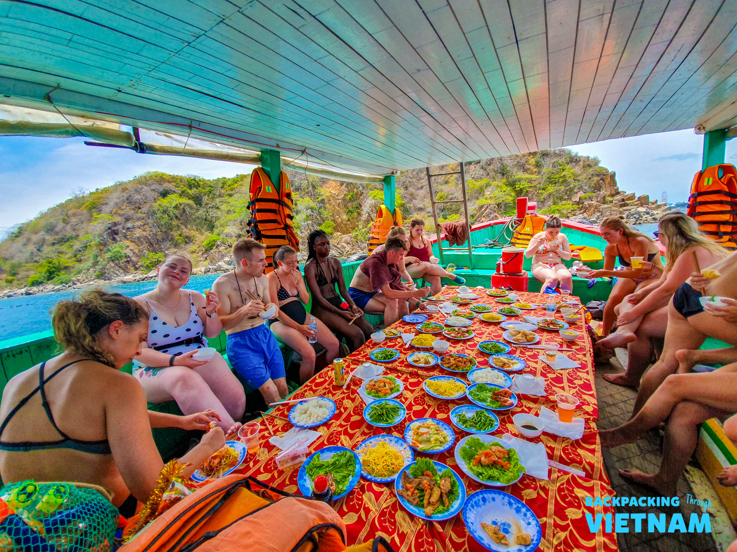 Happy backpackers enjoy a vibrant spread of local food on a boat tour in Nha Trang, Vietnam.