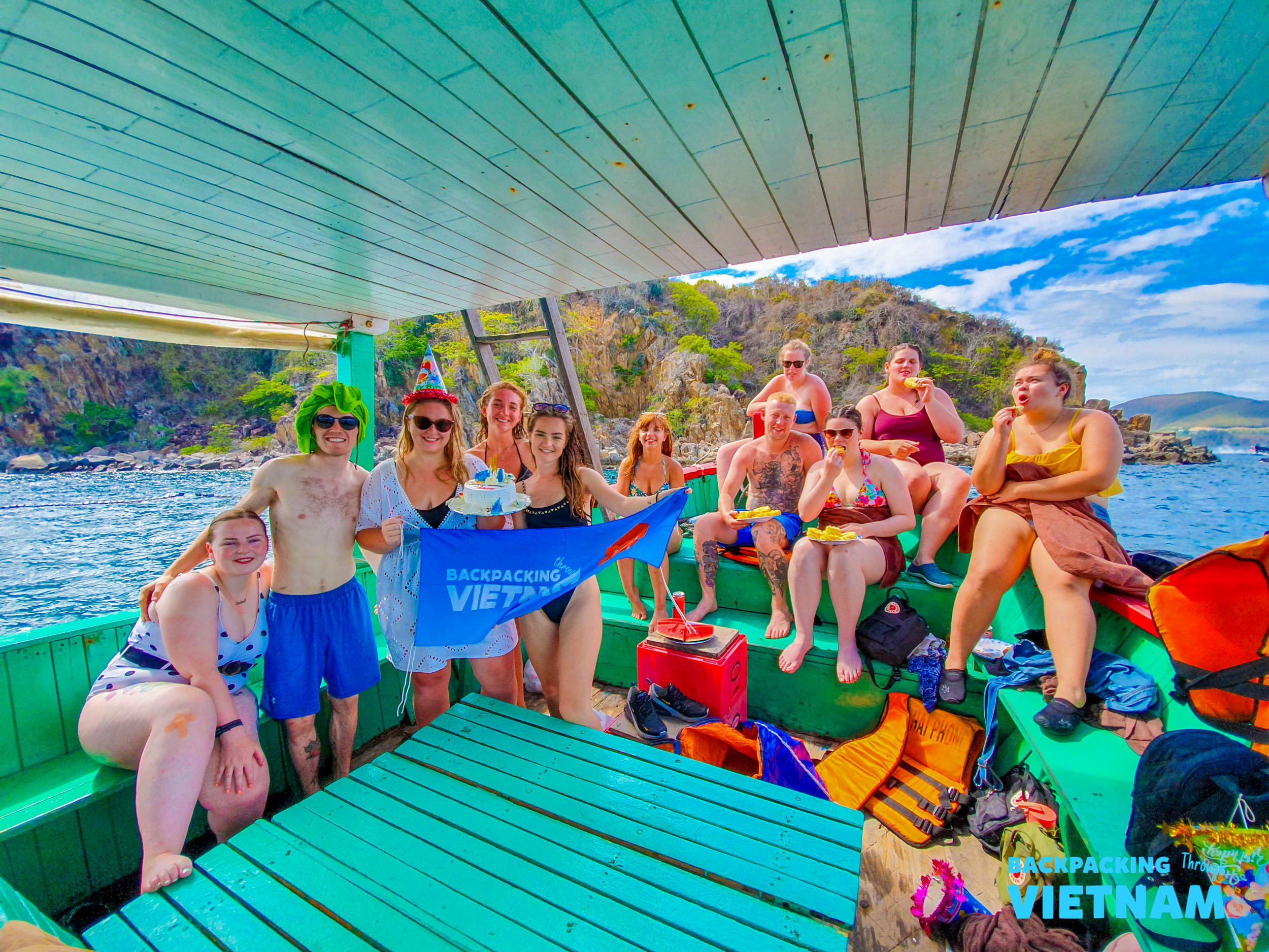 A group of happy backpackers celebrating on a boat during an island-hopping tour in Nha Trang, Vietnam.