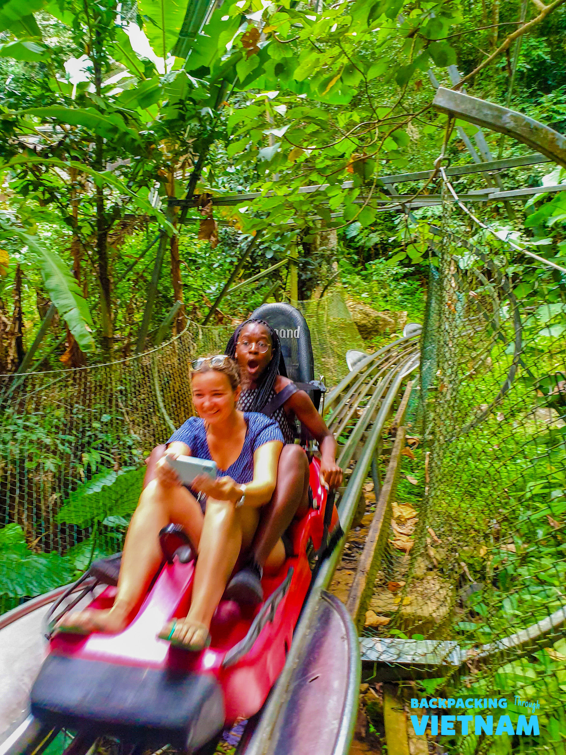 Two excited travelers ride an alpine coaster through lush green jungle in Dalat, Vietnam.