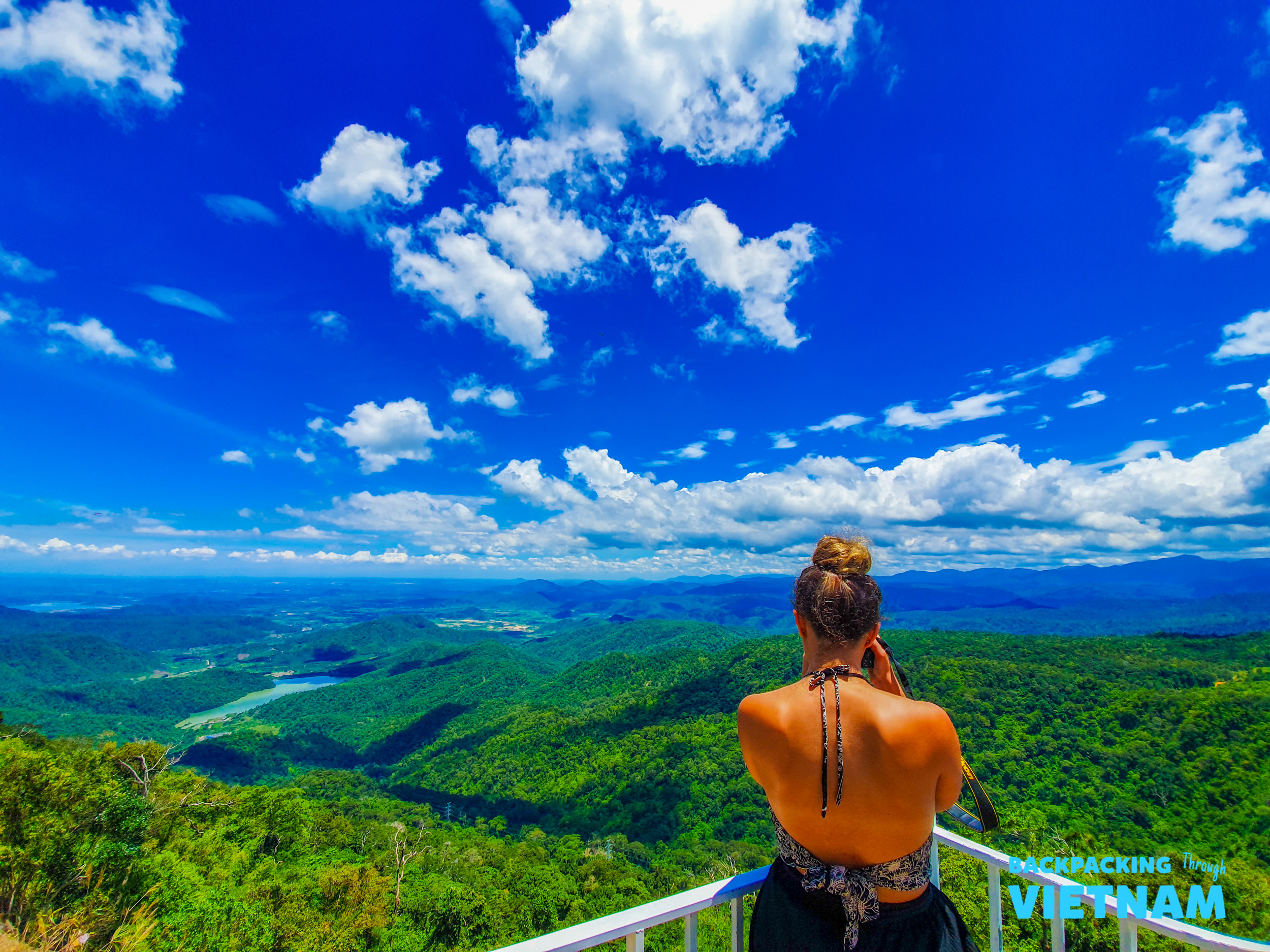 A woman admires the stunning green mountain landscape under a vibrant blue sky in Dalat, Vietnam.