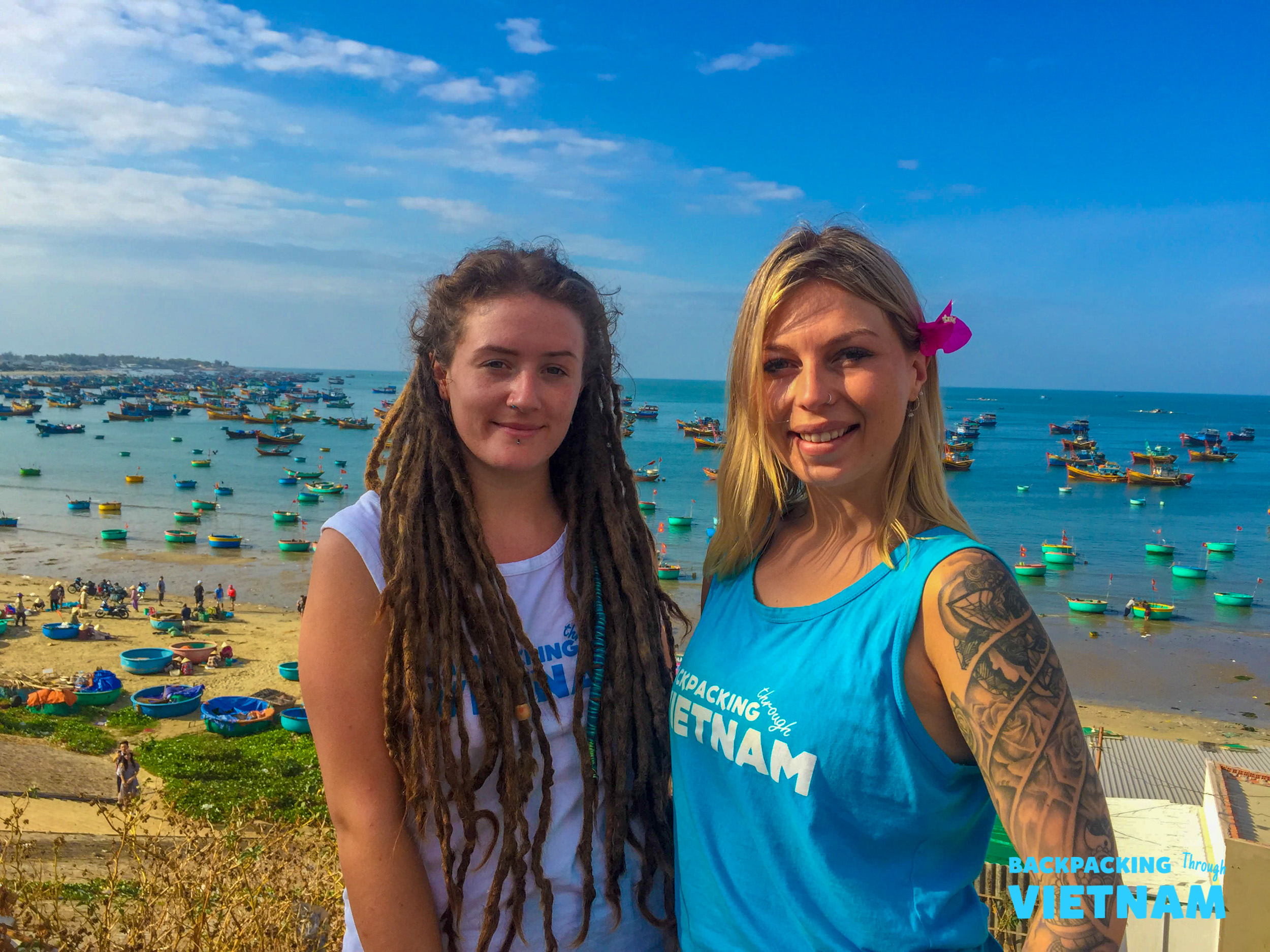 Two happy women overlook Mui Ne fishing village with numerous colorful boats on the beach.