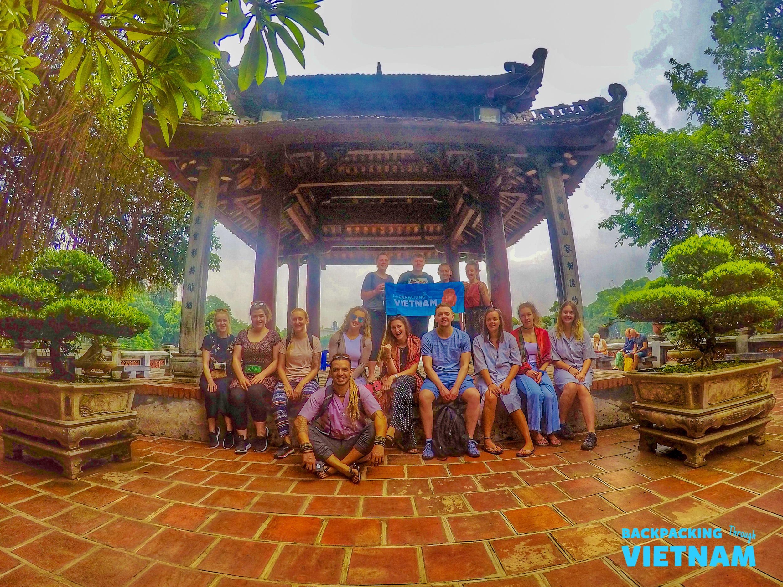A group of happy backpackers pose for a photo in front of a traditional Vietnamese pavilion in Hanoi.