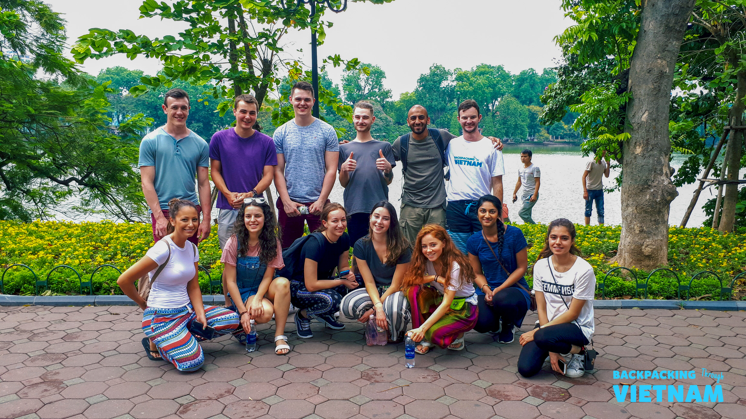 Happy travelers pose for a group photo in a scenic park beside a lake in Hanoi.