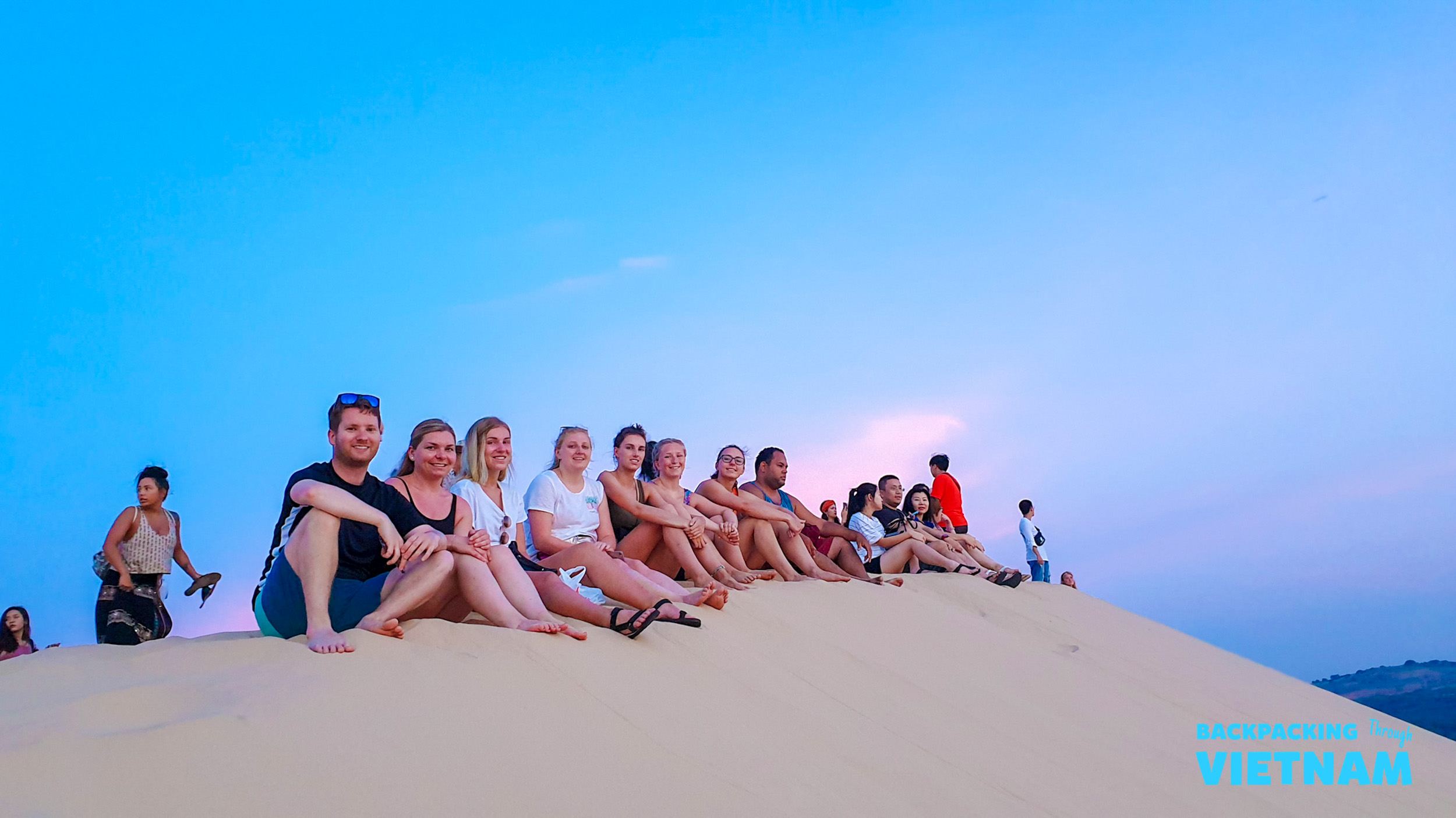 A group of friends enjoys the sunrise from the top of a sand dune in Mui Ne, Vietnam.
