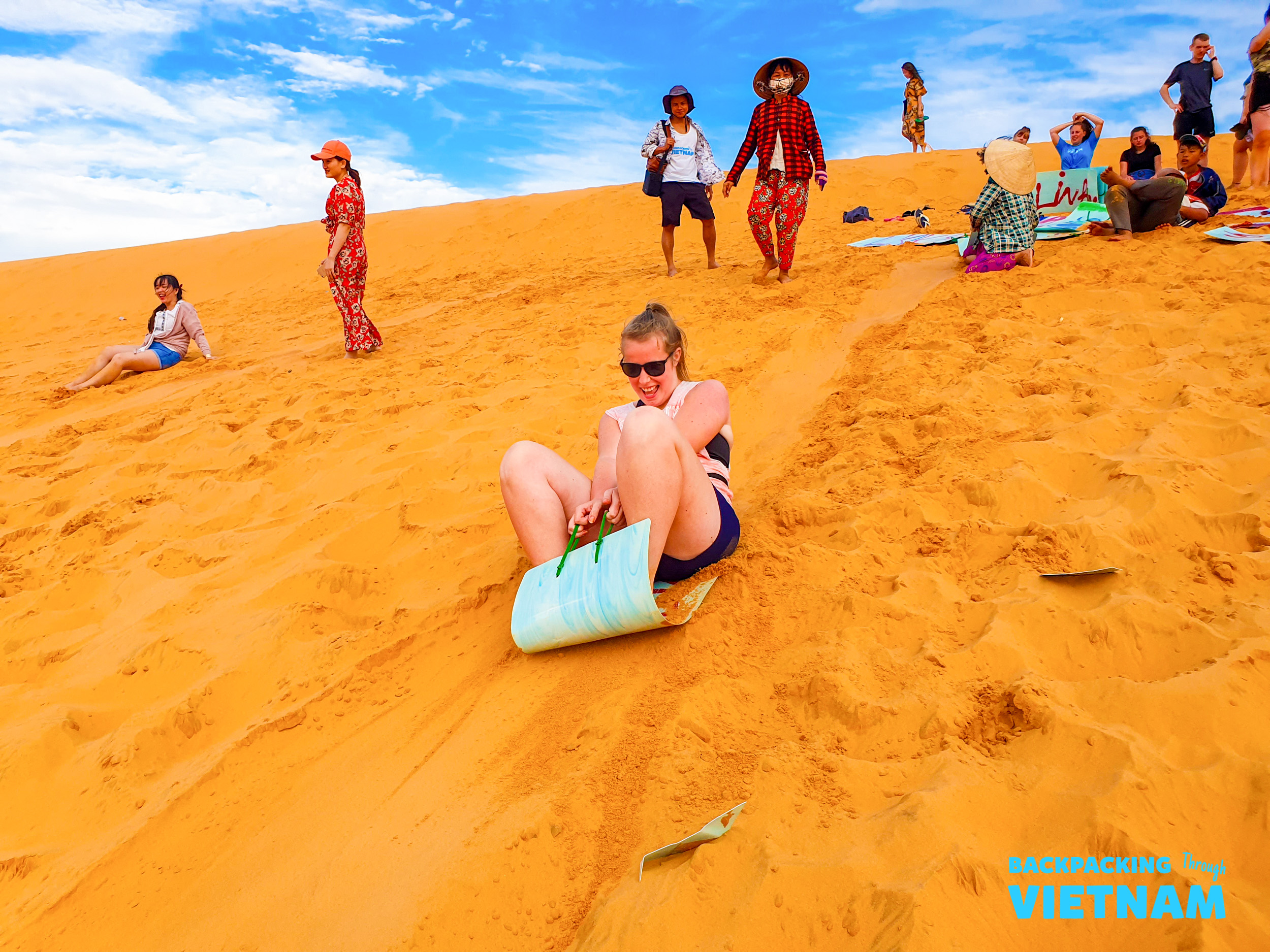 A young woman joyfully sand sleds down the vibrant red dunes of Mui Ne, Vietnam.