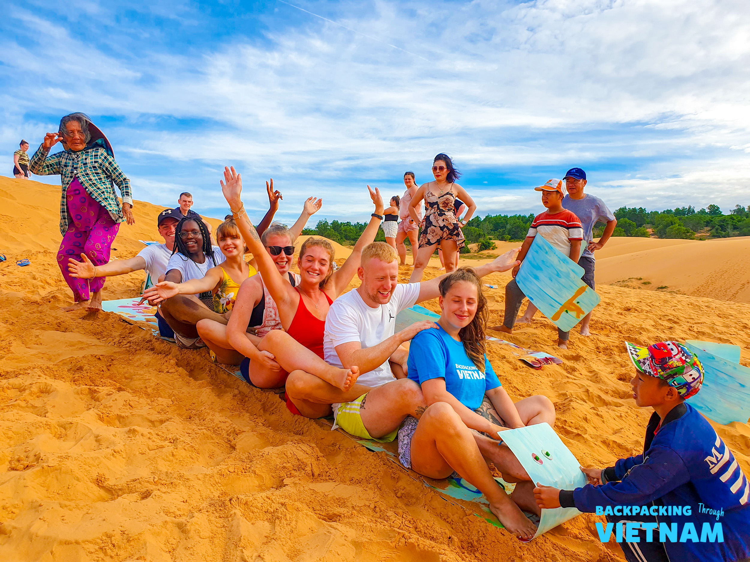 Backpacking group sand sledding down white dunes in Mui Ne