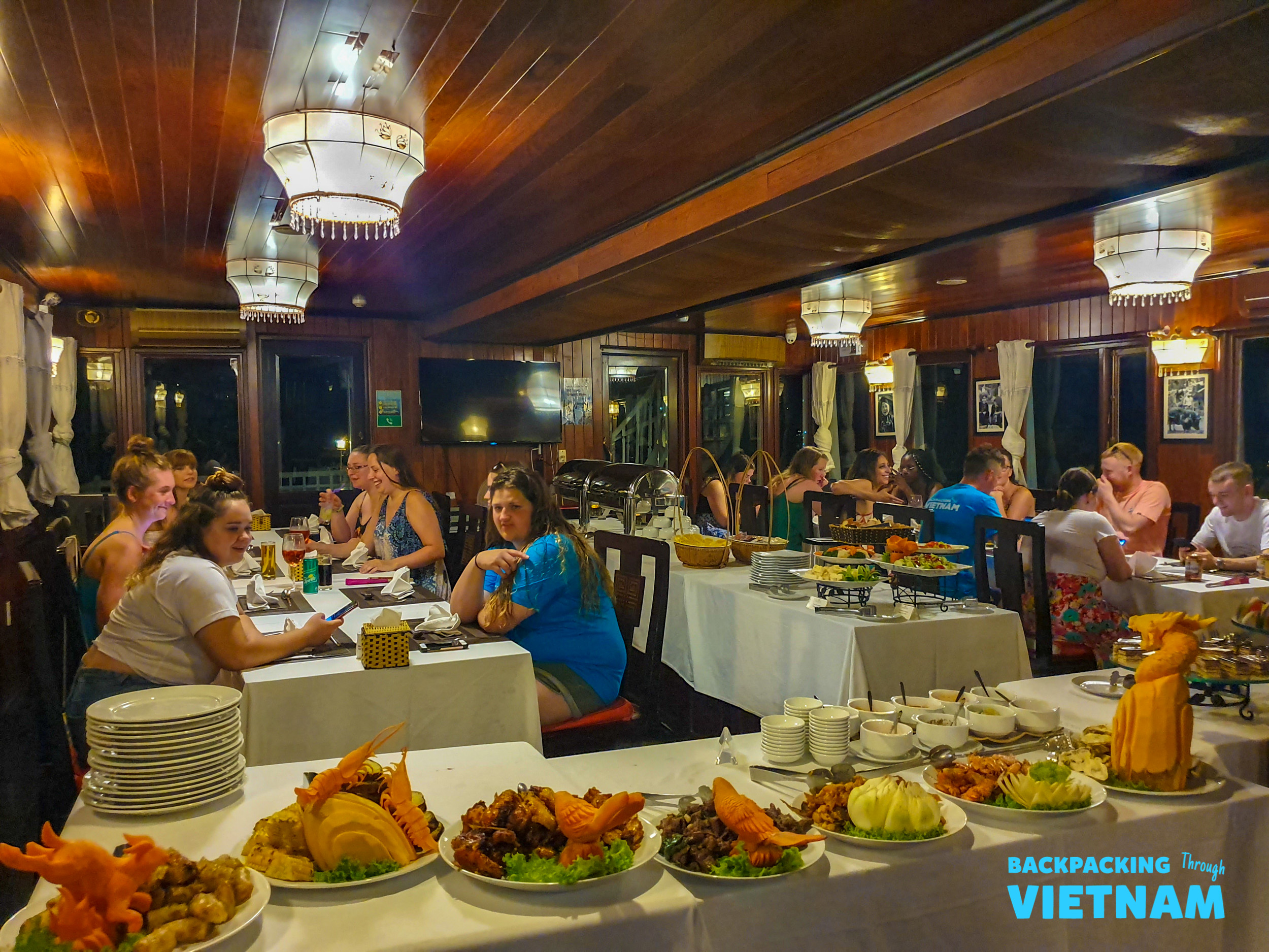 Travelers enjoy a delicious buffet dinner inside a sleeper boat while cruising Halong Bay, Vietnam.