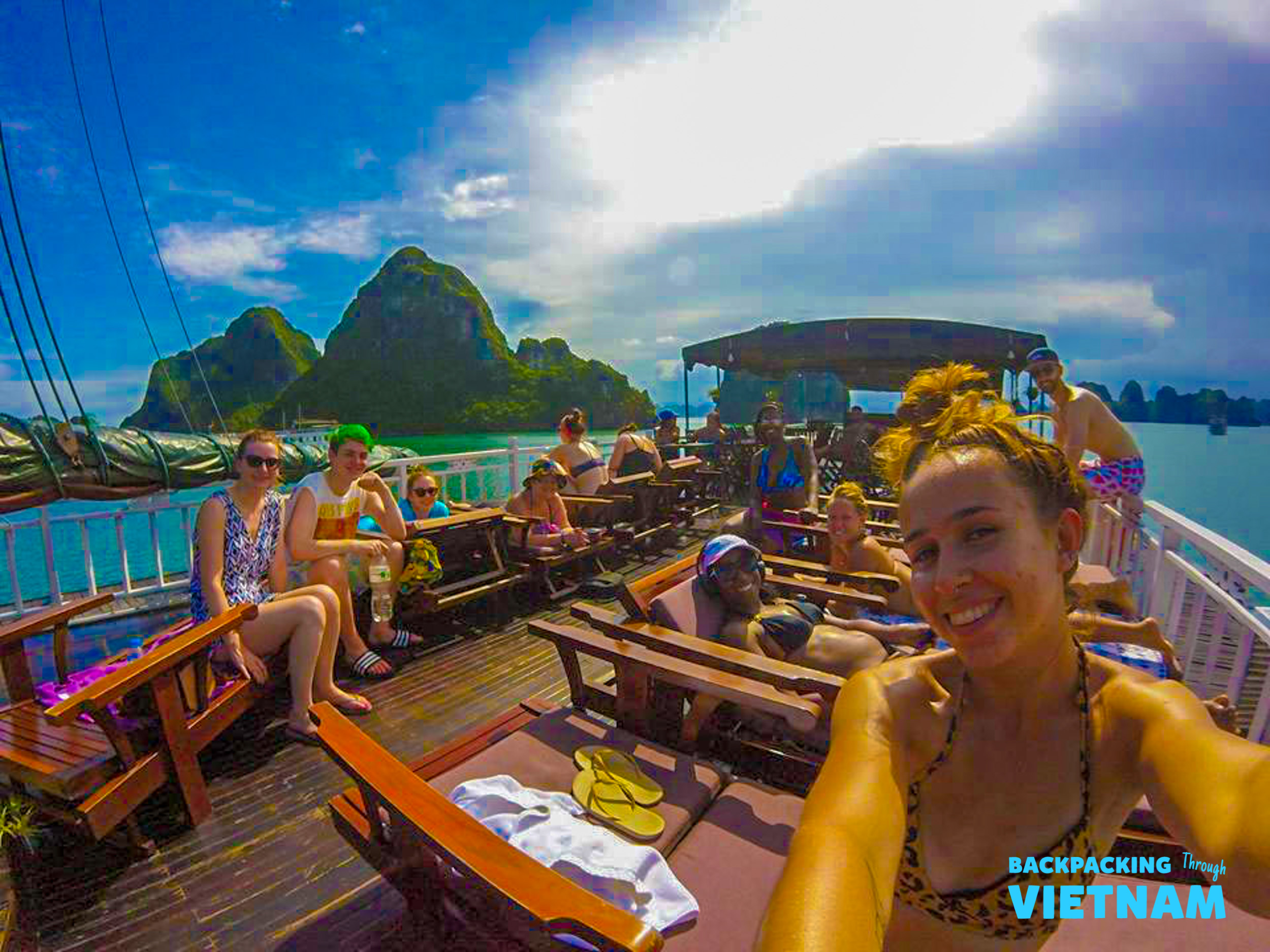 Smiling backpackers lounge on a boat deck, surrounded by the majestic islands of Halong Bay, Vietnam.