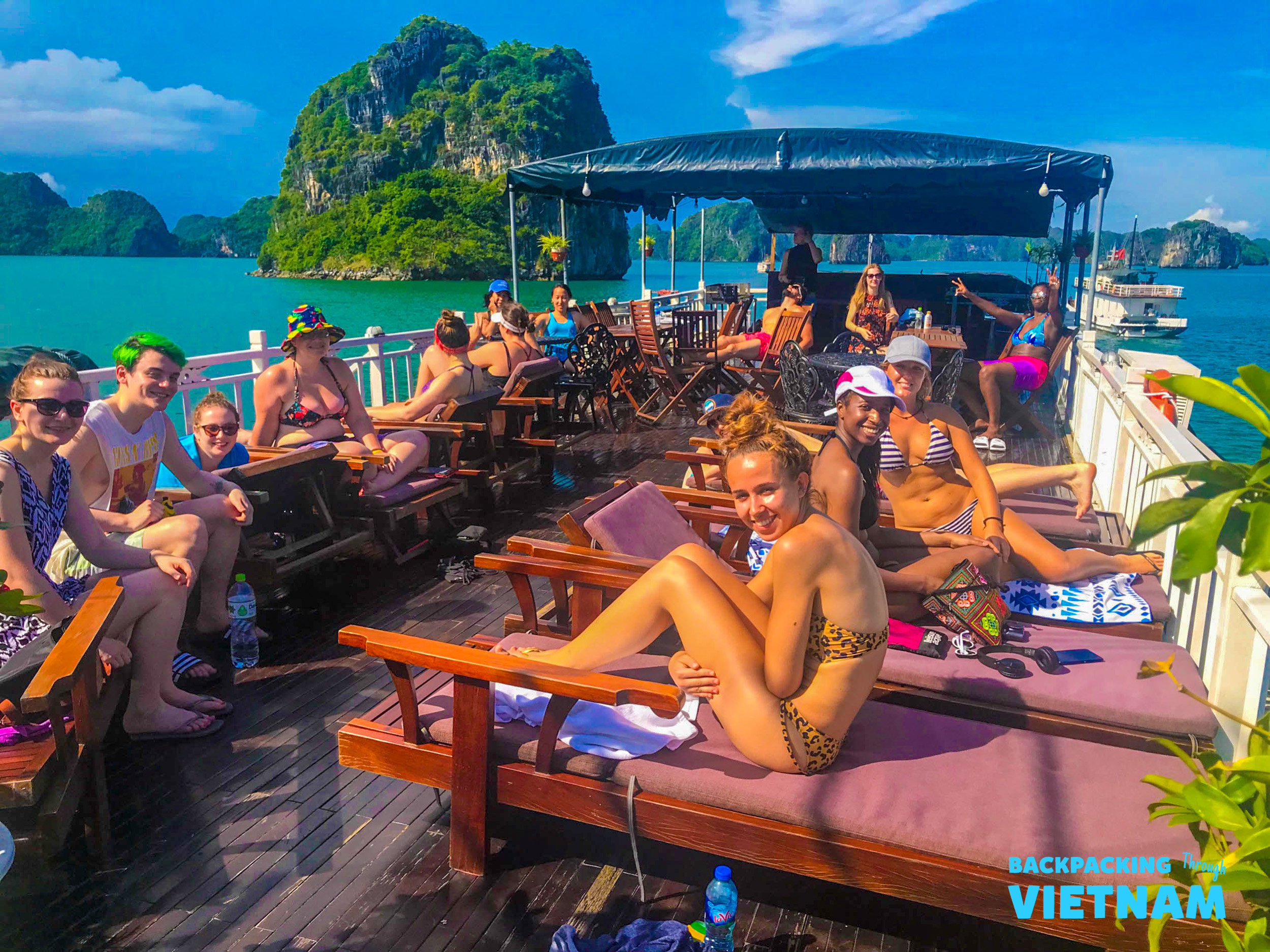 Happy backpackers relax on a boat deck, cruising through the beautiful limestone karsts of Halong Bay, Vietnam.