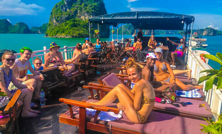 Happy backpackers relax on a boat deck, cruising through the beautiful limestone karsts of Halong Bay, Vietnam.