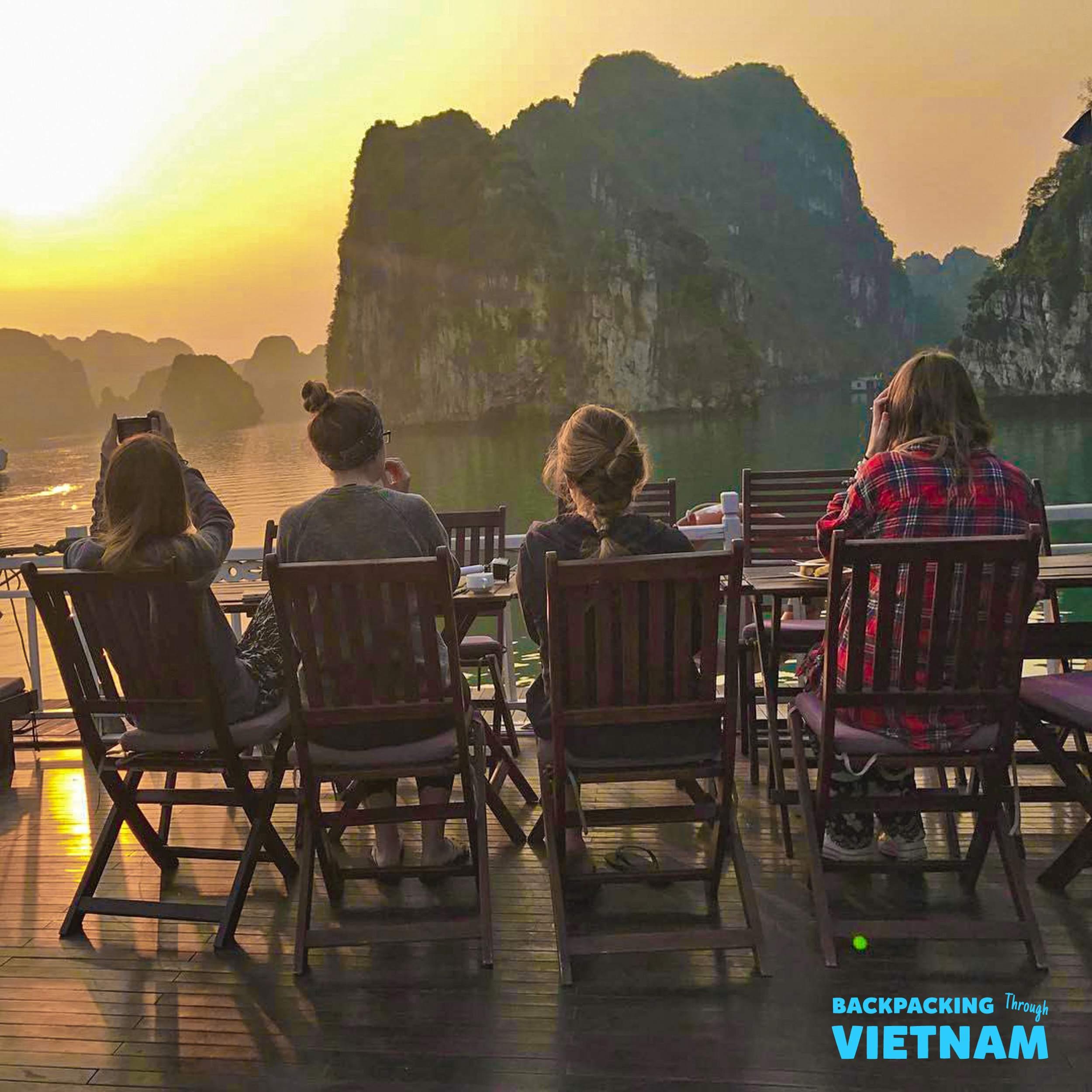 Four friends watch a beautiful sunset over the stunning limestone karsts of Halong Bay, Vietnam.