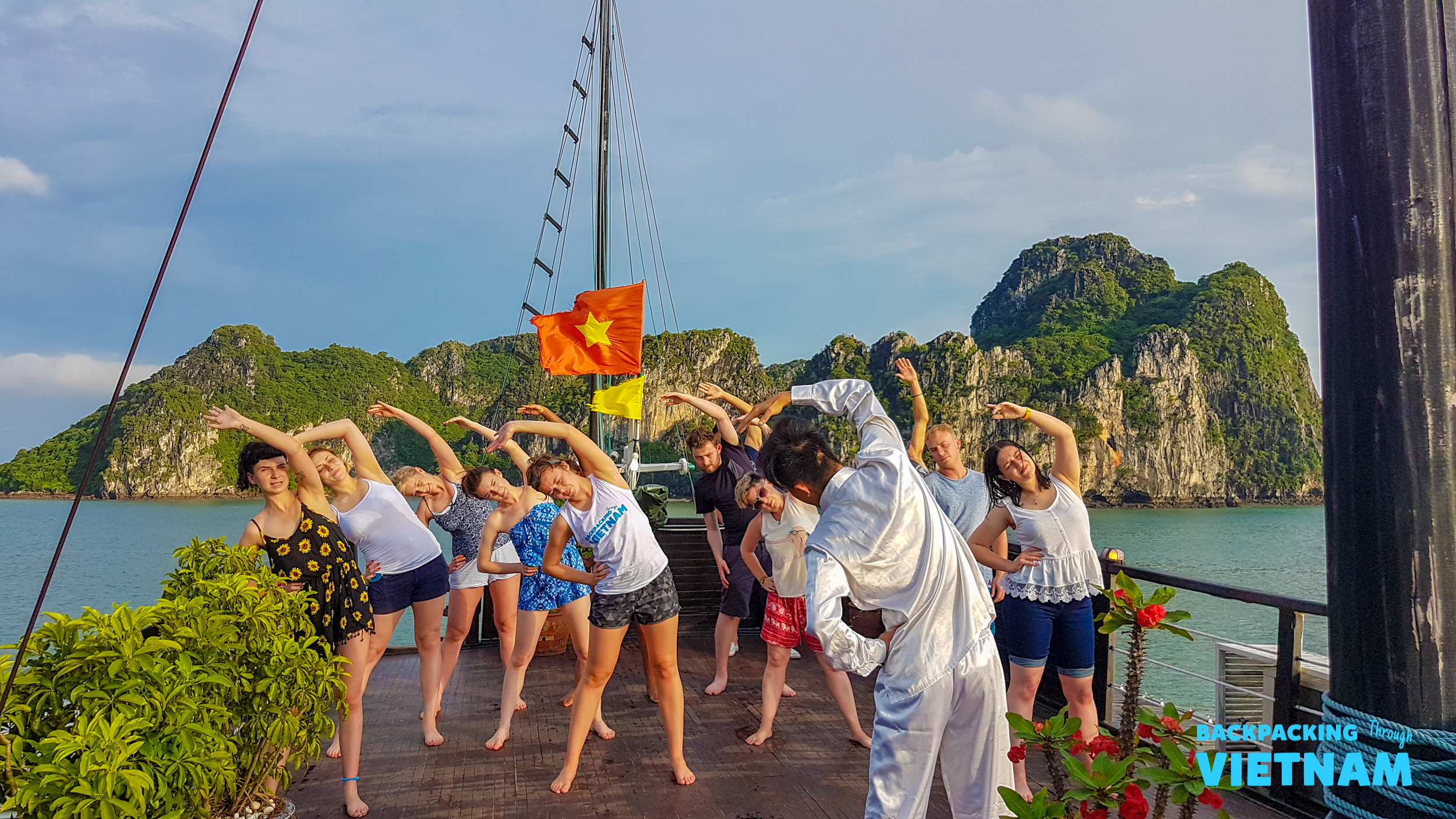Travelers enjoy a morning yoga session on a boat deck amidst the stunning Halong Bay karst islands.