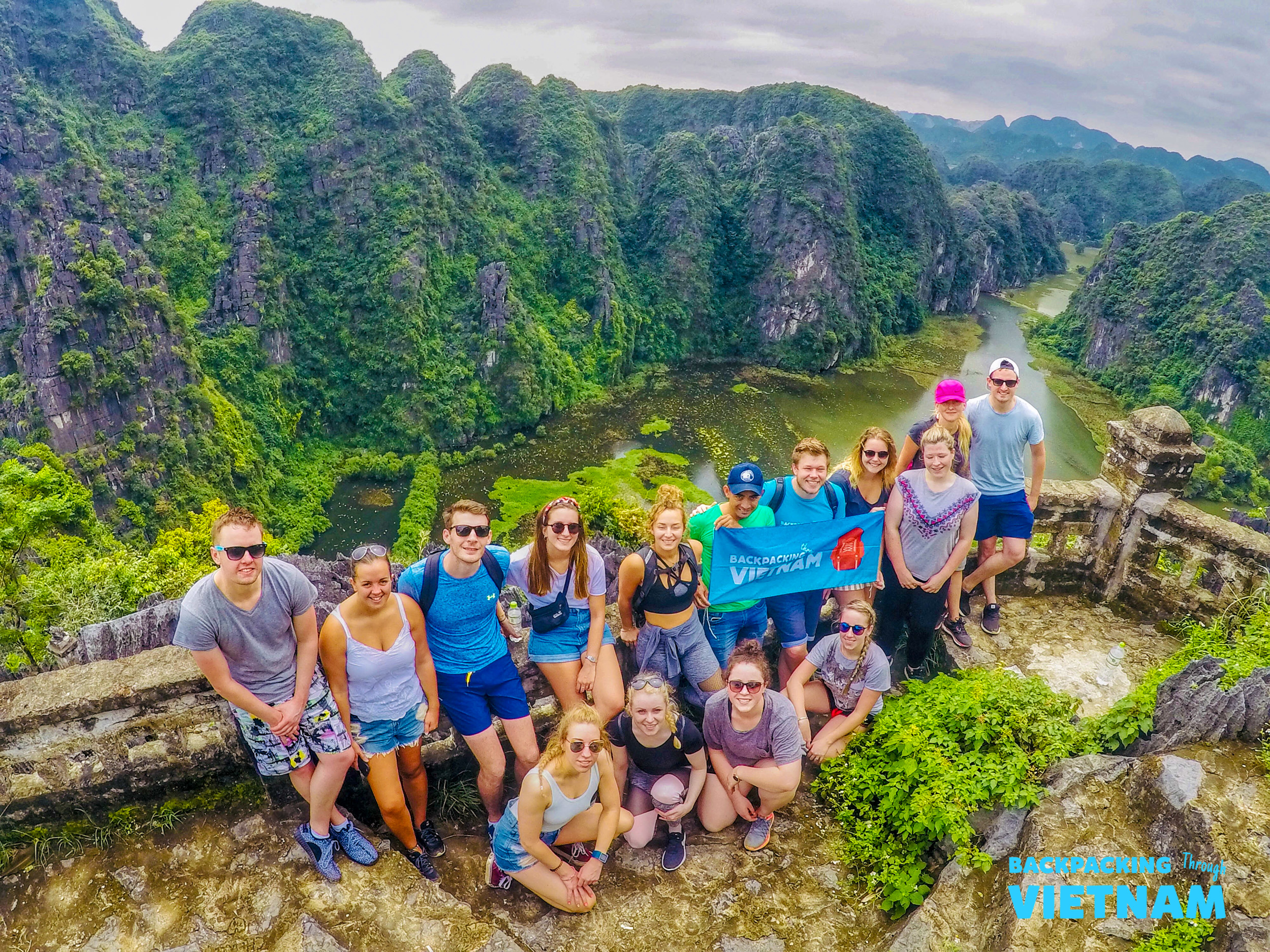 Smiling backpackers gather on a mountain peak, enjoying the breathtaking view of Tam Coc's rivers and karsts.