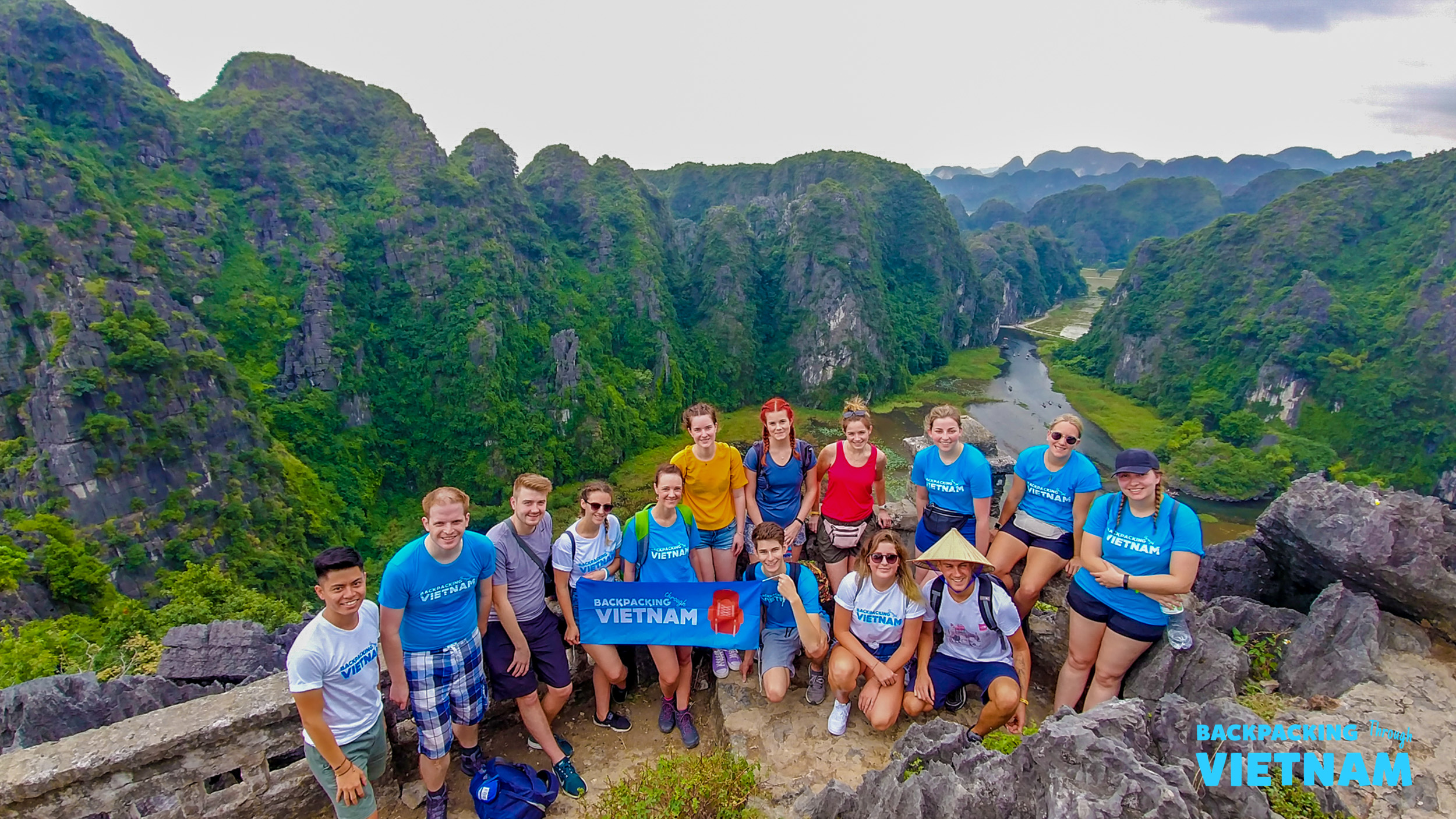Happy backpackers pose at the summit of Lying Dragon Mountain, overlooking the stunning Tam Coc landscape.
