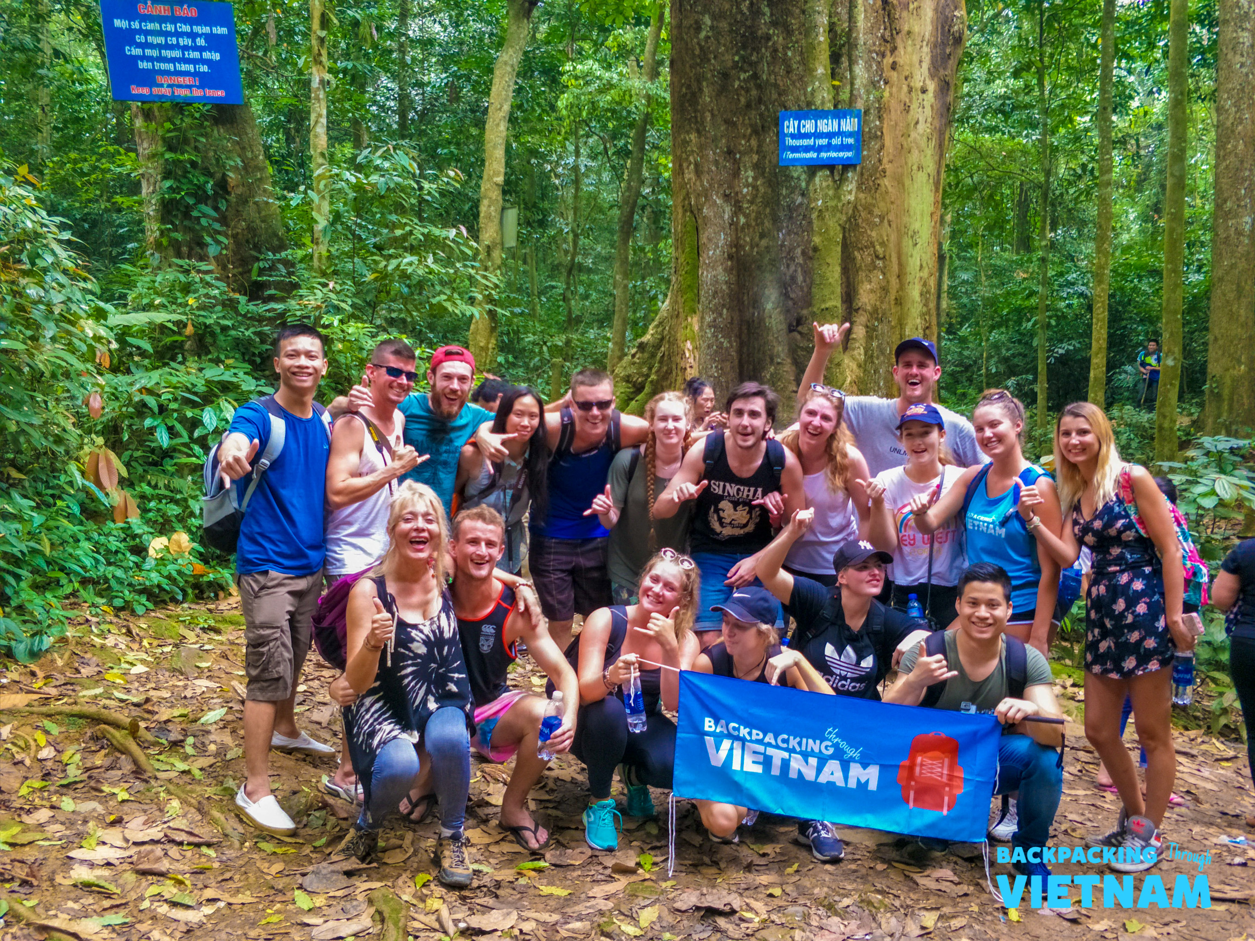 A large group of happy backpackers posing in the lush jungle of Phong Nha, Vietnam.