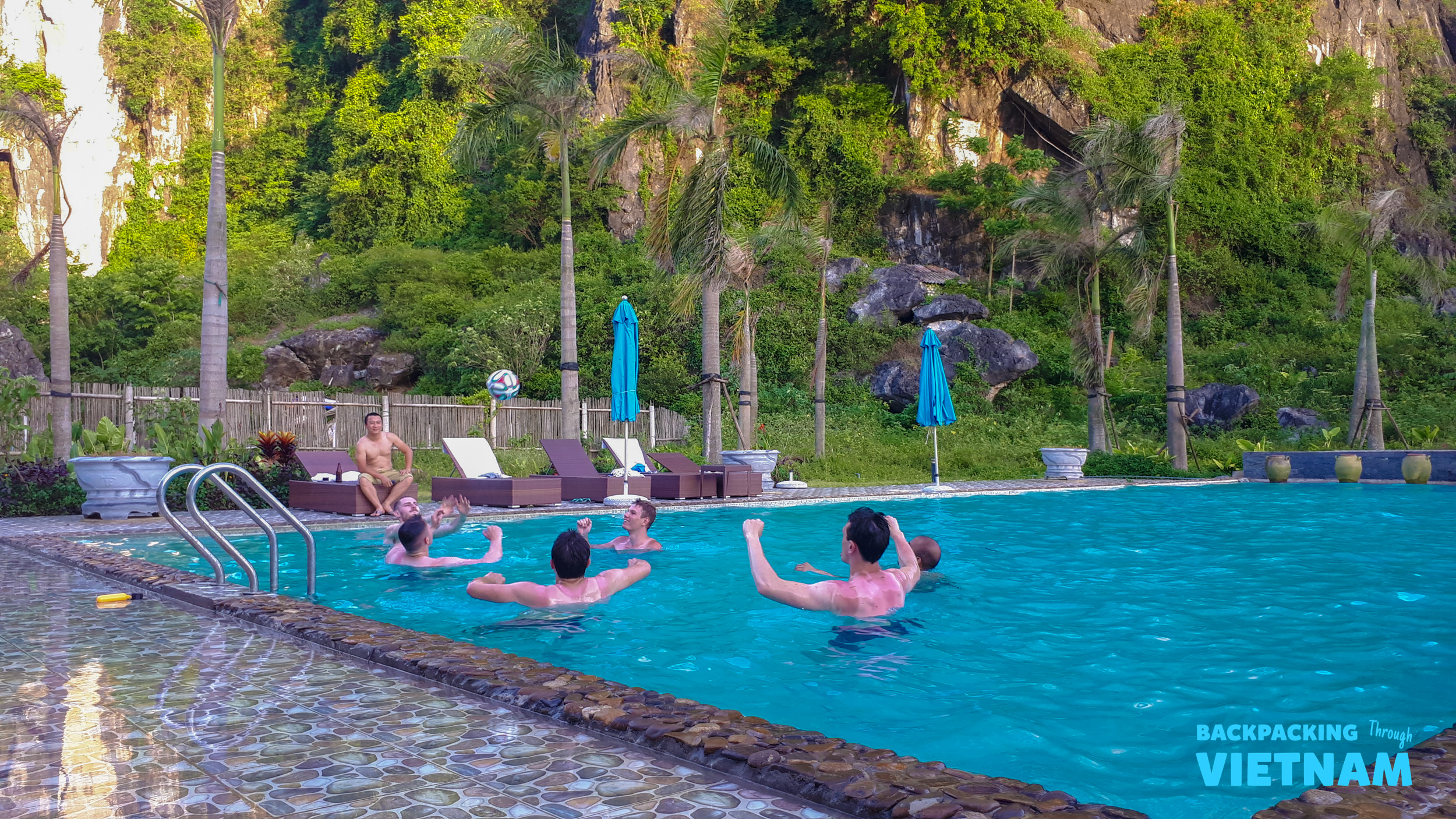 Backpackers enjoy a refreshing swim in a resort pool surrounded by lush Phong Nha mountains.