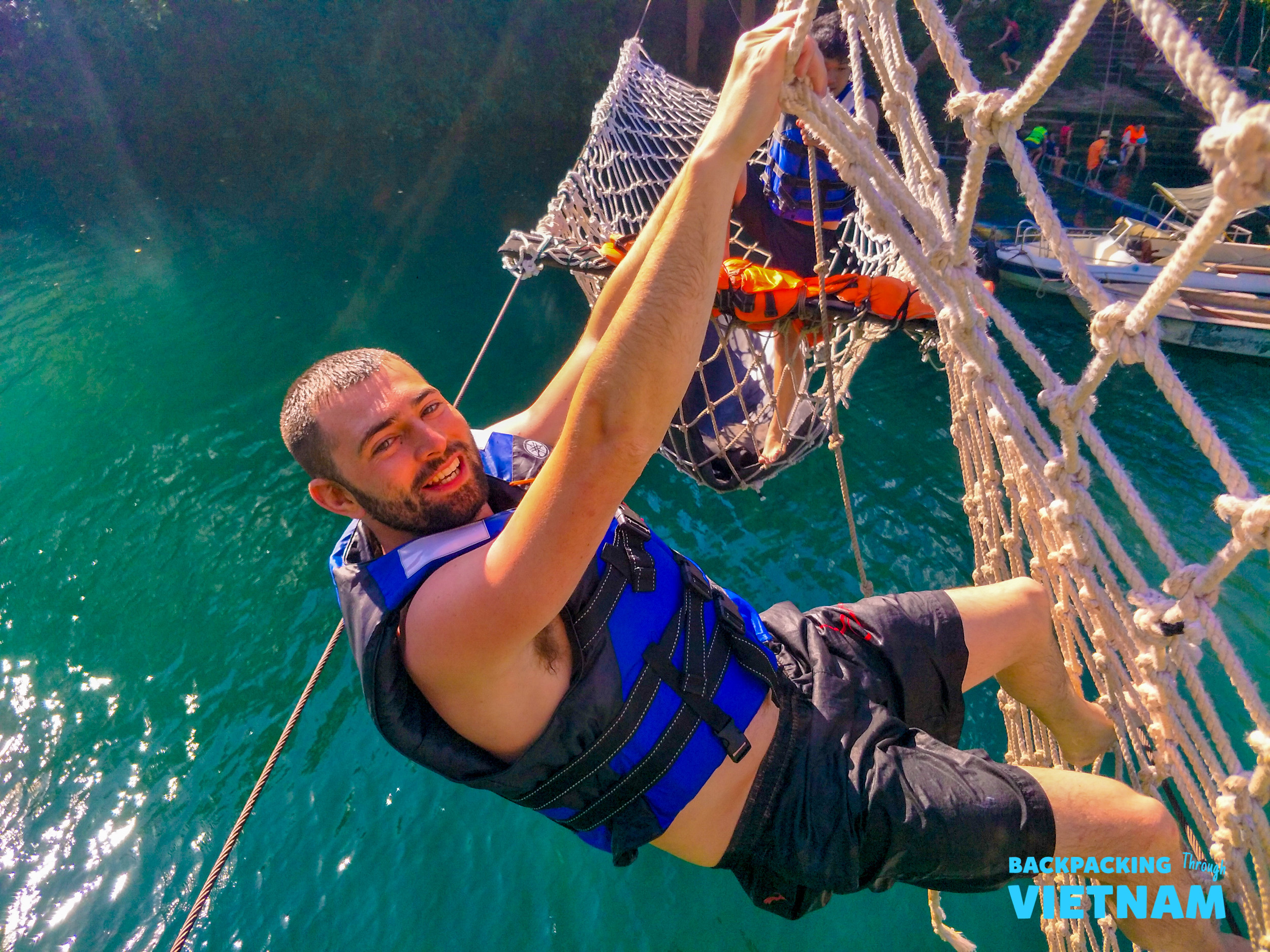 Adventurous man in a life vest climbs a rope net over the beautiful waters of Phong Nha.