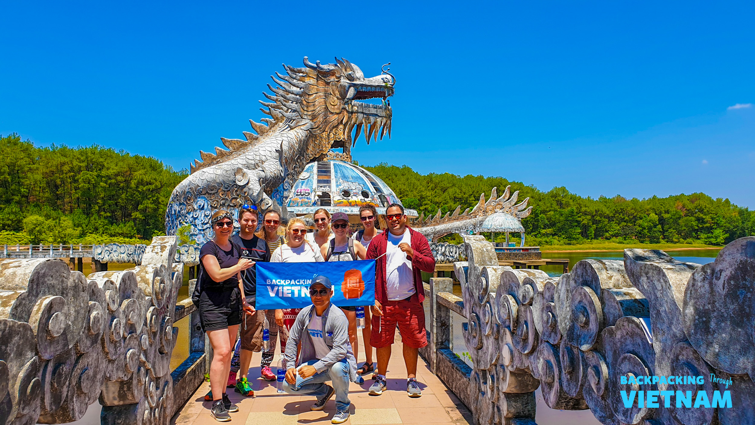 Backpackers pose with their flag in front of the impressive abandoned dragon structure in Hue, Vietnam.