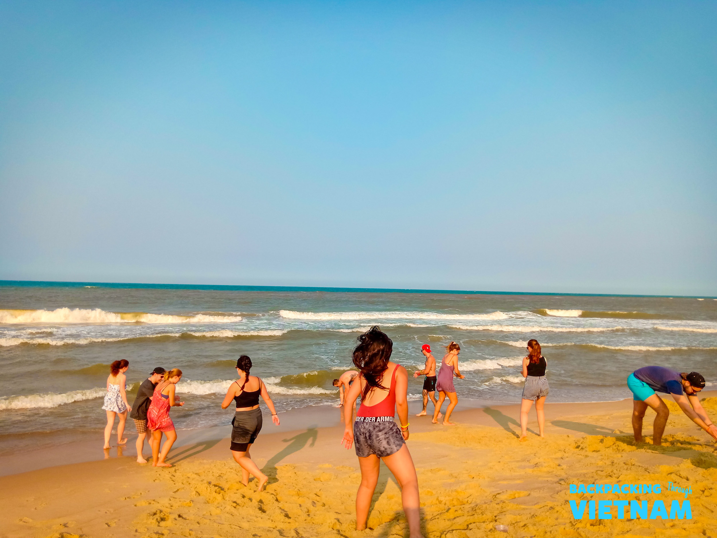Backpackers enjoy a sunny beach day in Vietnam, playing in the sand and near the ocean waves.