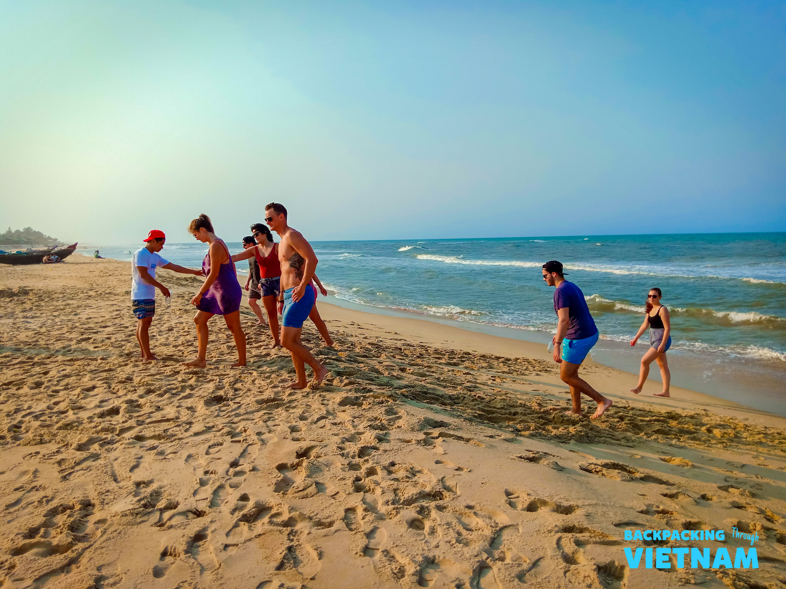 Backpackers enjoy a sunny day on a wide sandy beach in Vietnam, walking and playing.