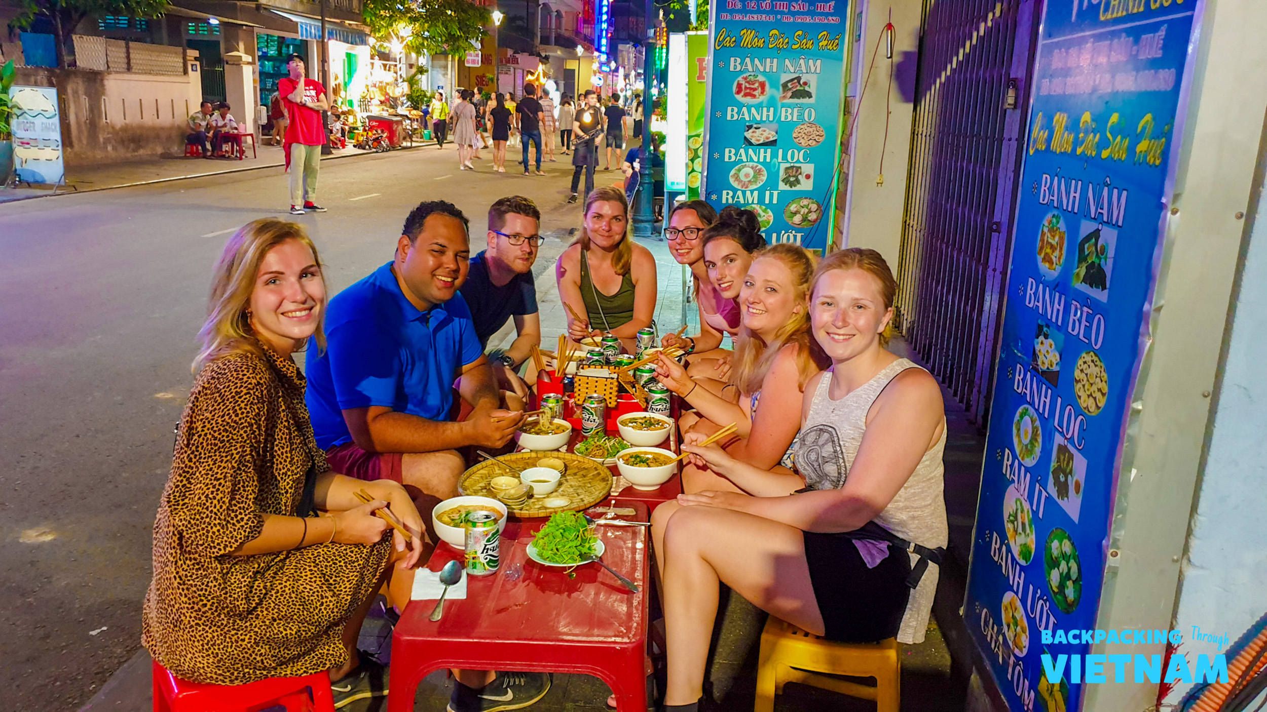 A group of happy backpackers enjoying a delicious street food meal together in Hue, Vietnam.