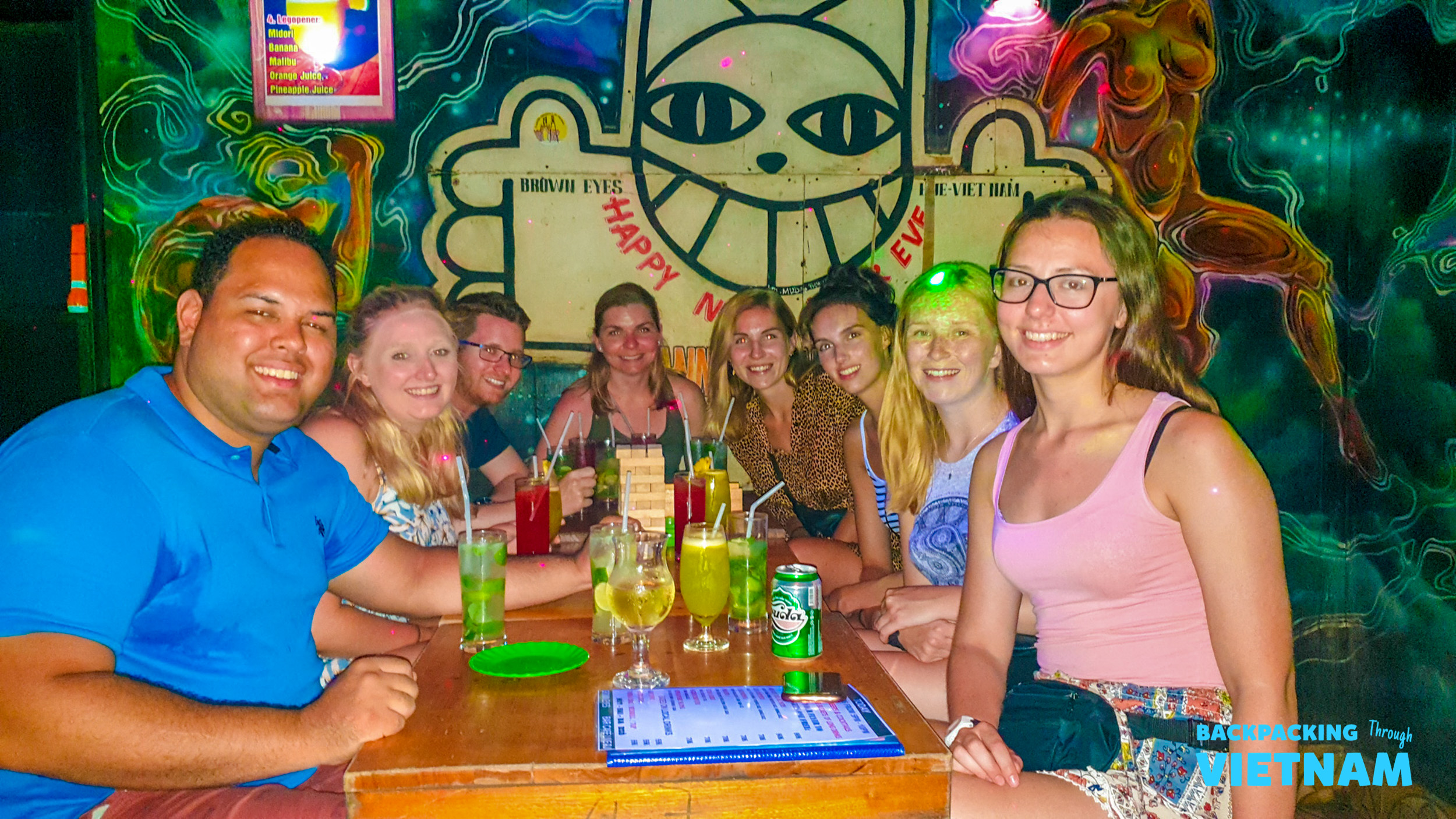 A happy group of backpackers enjoying drinks at a vibrant, neon-lit bar in Hue, Vietnam.