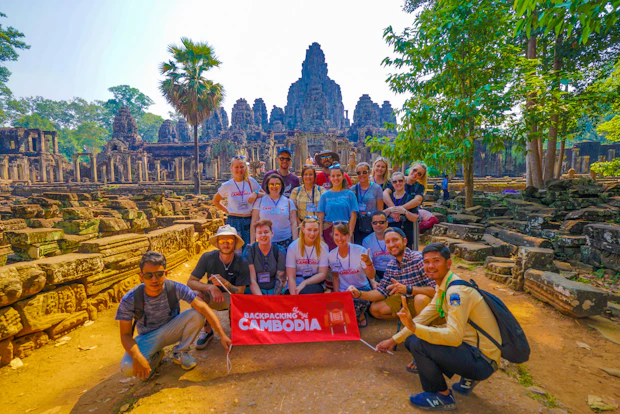 A group of happy backpackers pose with a banner in front of the ancient Bayon temple, Cambodia.