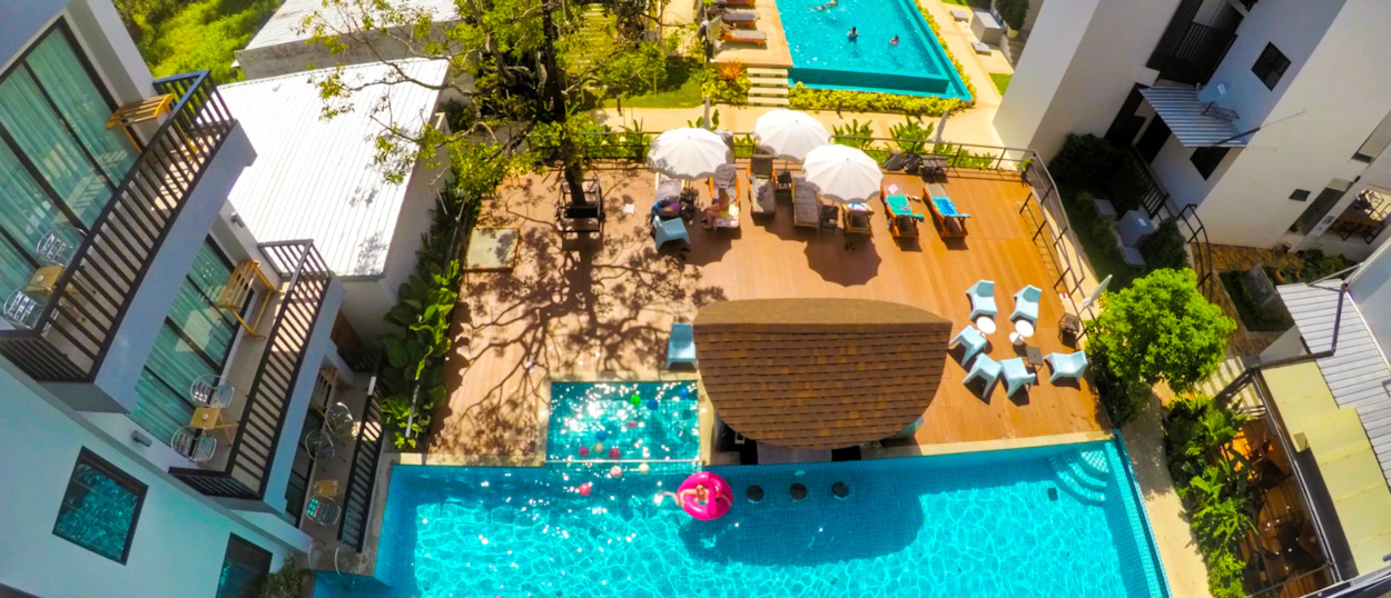 Aerial view of a vibrant Krabi resort with multiple pools, sun loungers, and guests relaxing.