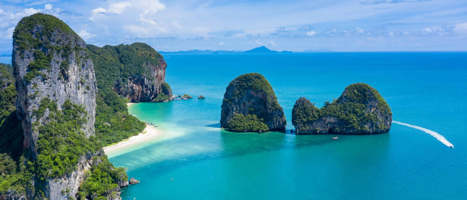Aerial view of Krabi's stunning coastline, featuring limestone islands, a white beach, and a boat on turquoise water.
