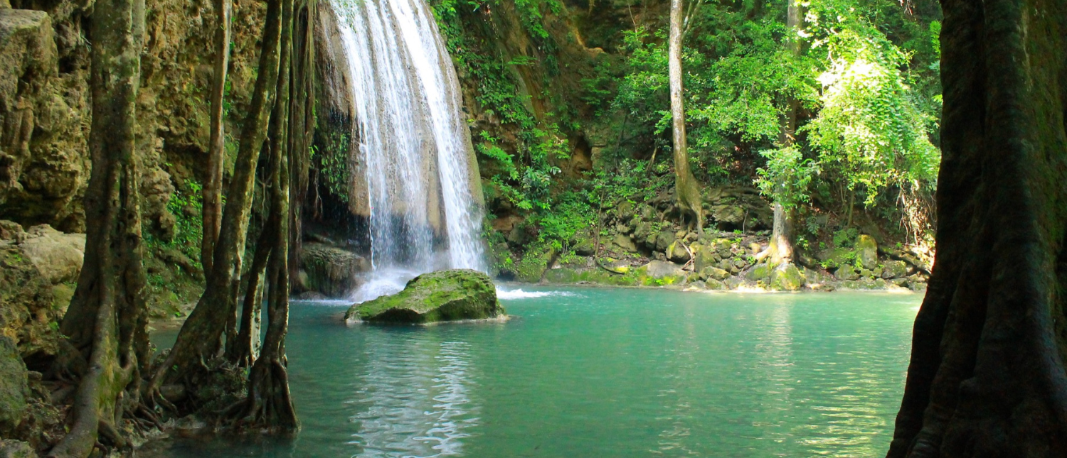 A beautiful waterfall cascades into an emerald pool surrounded by lush jungle at Erawan National Park.