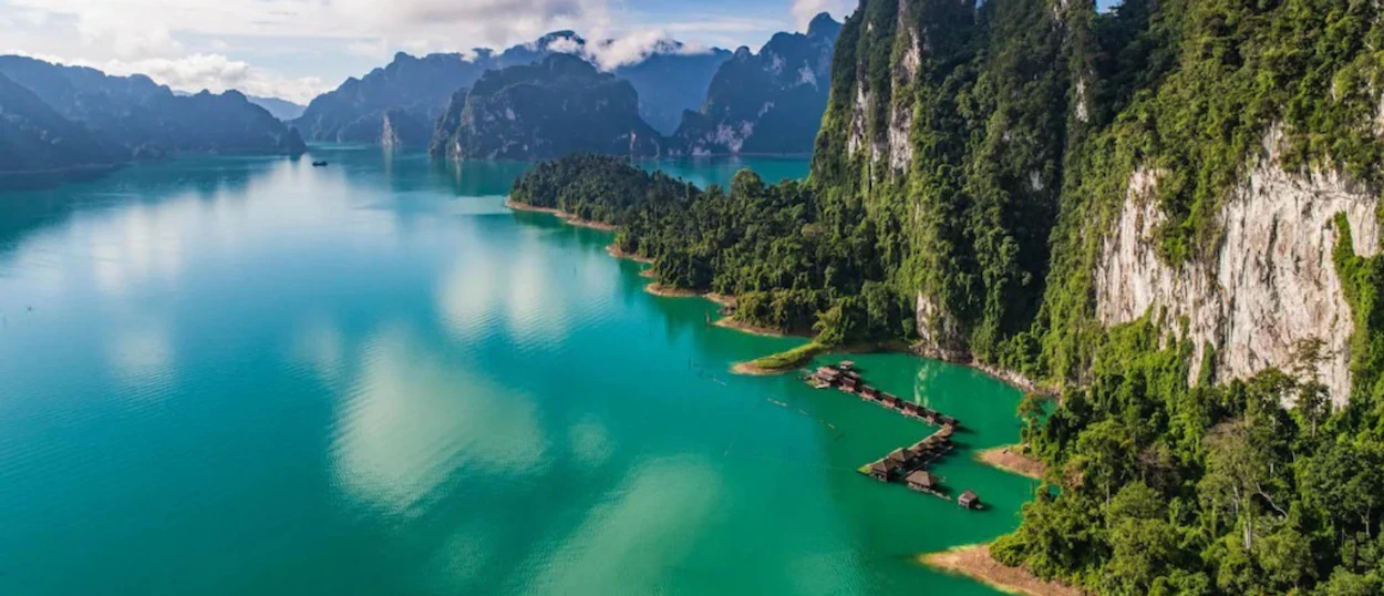 Floating bungalows on Cheow Lan Lake's turquoise waters, surrounded by towering jungle-covered limestone karsts.
