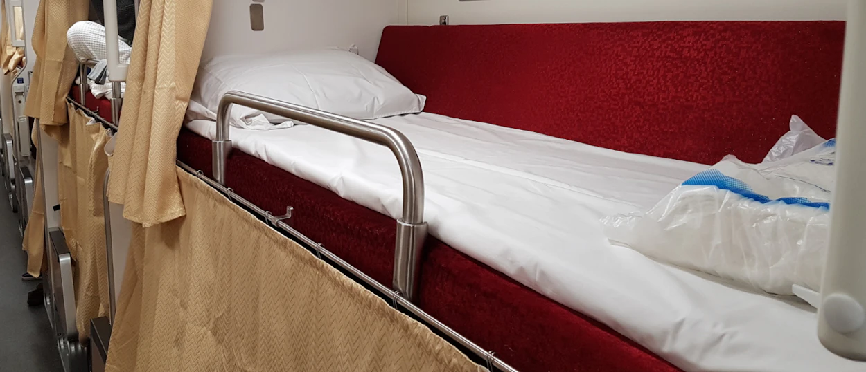 A clean, comfortable bunk bed with a red mattress and white sheets on a Thai sleeper train.