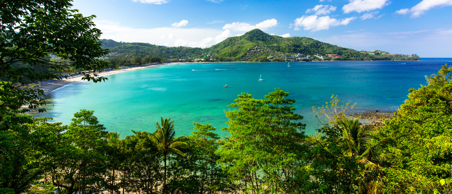 Panoramic view of Patong Beach in Phuket, Thailand, with clear turquoise water and lush hills.