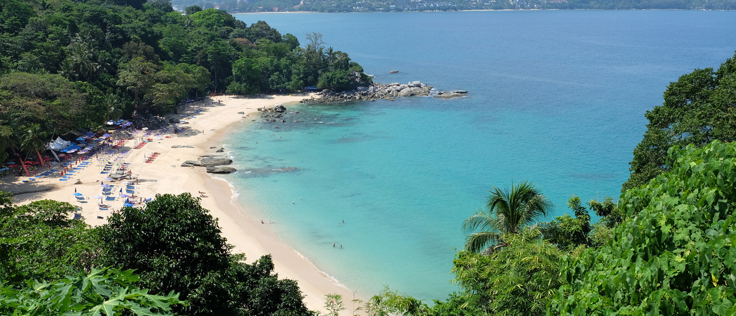 A beautiful secluded beach in Phuket with turquoise water, white sand, and lush green trees.