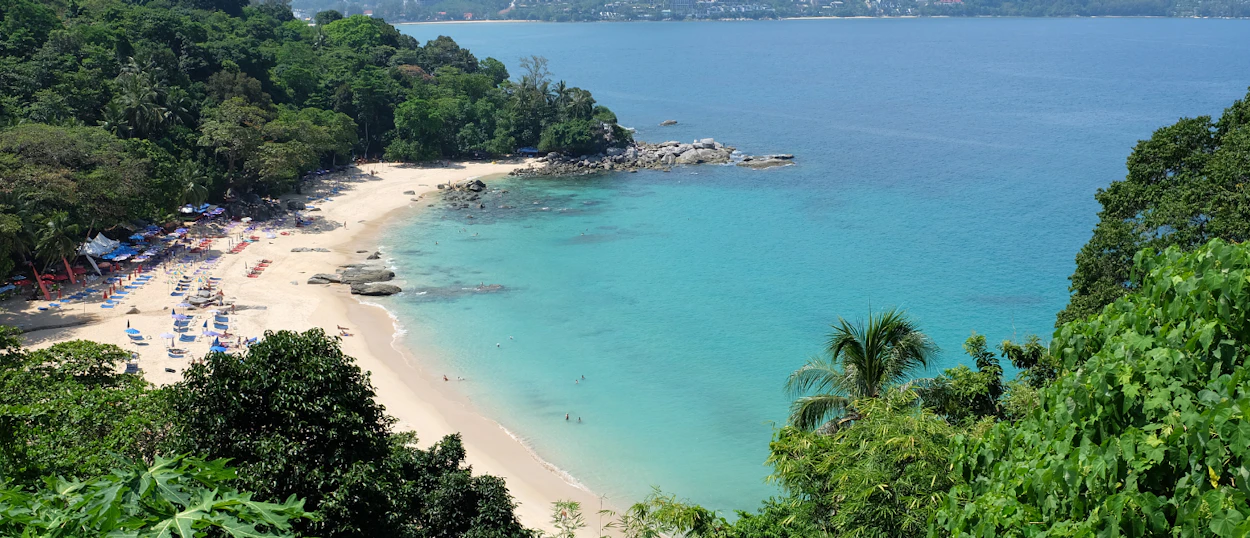 A beautiful secluded beach in Phuket with turquoise water, white sand, and lush green trees.