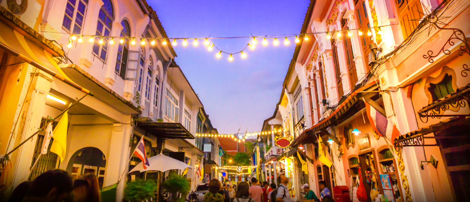 Colorful Sino-Portuguese buildings line a bustling street in Phuket Old Town, lit by festive string lights.