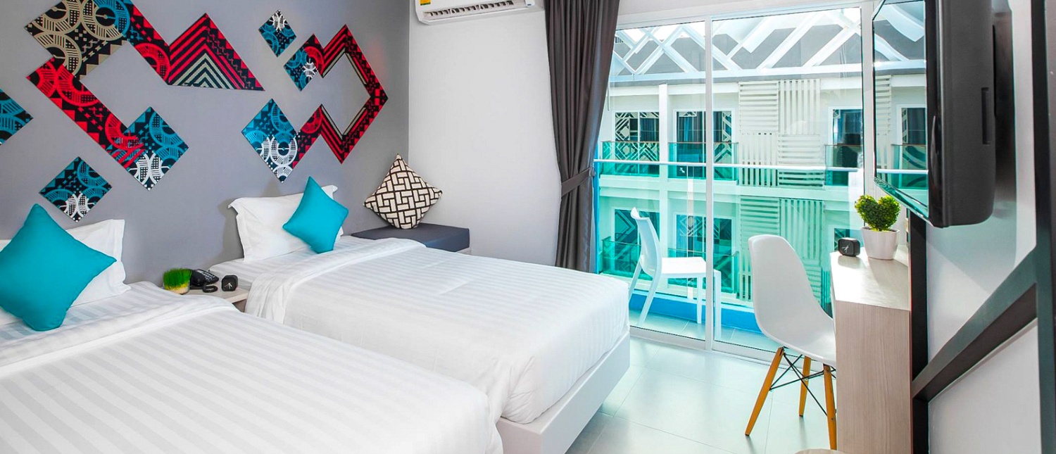 A modern hotel room in Phuket with two single beds, blue pillows, and a balcony.