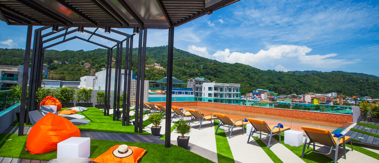 A sunny rooftop lounge in Phuket with bean bags, sun loungers, and a view of green mountains.