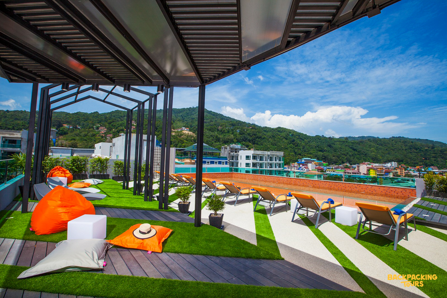 Relaxing rooftop terrace with sun loungers, bean bags, and scenic views of Phuket's green hills.