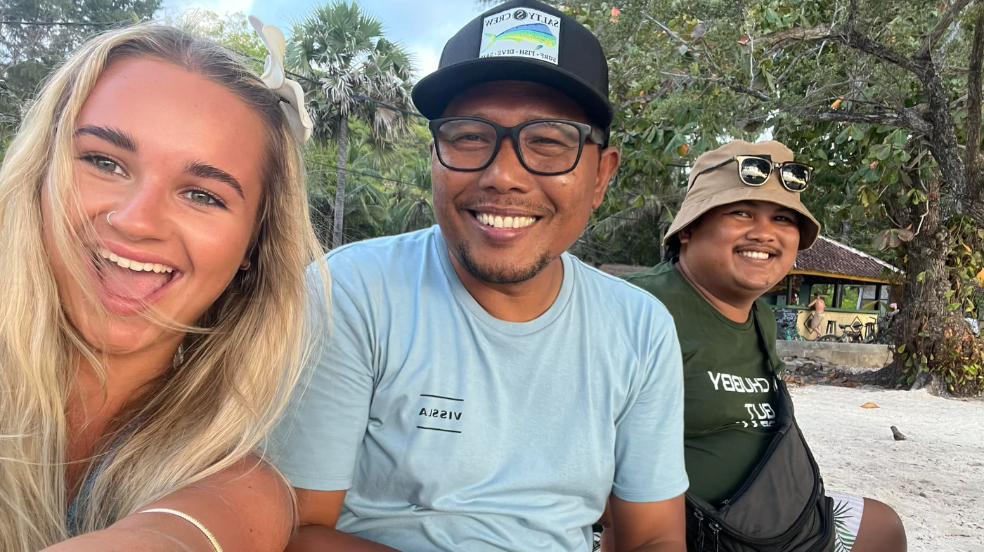 Three happy friends smiling for a selfie on a sandy beach in Bali.